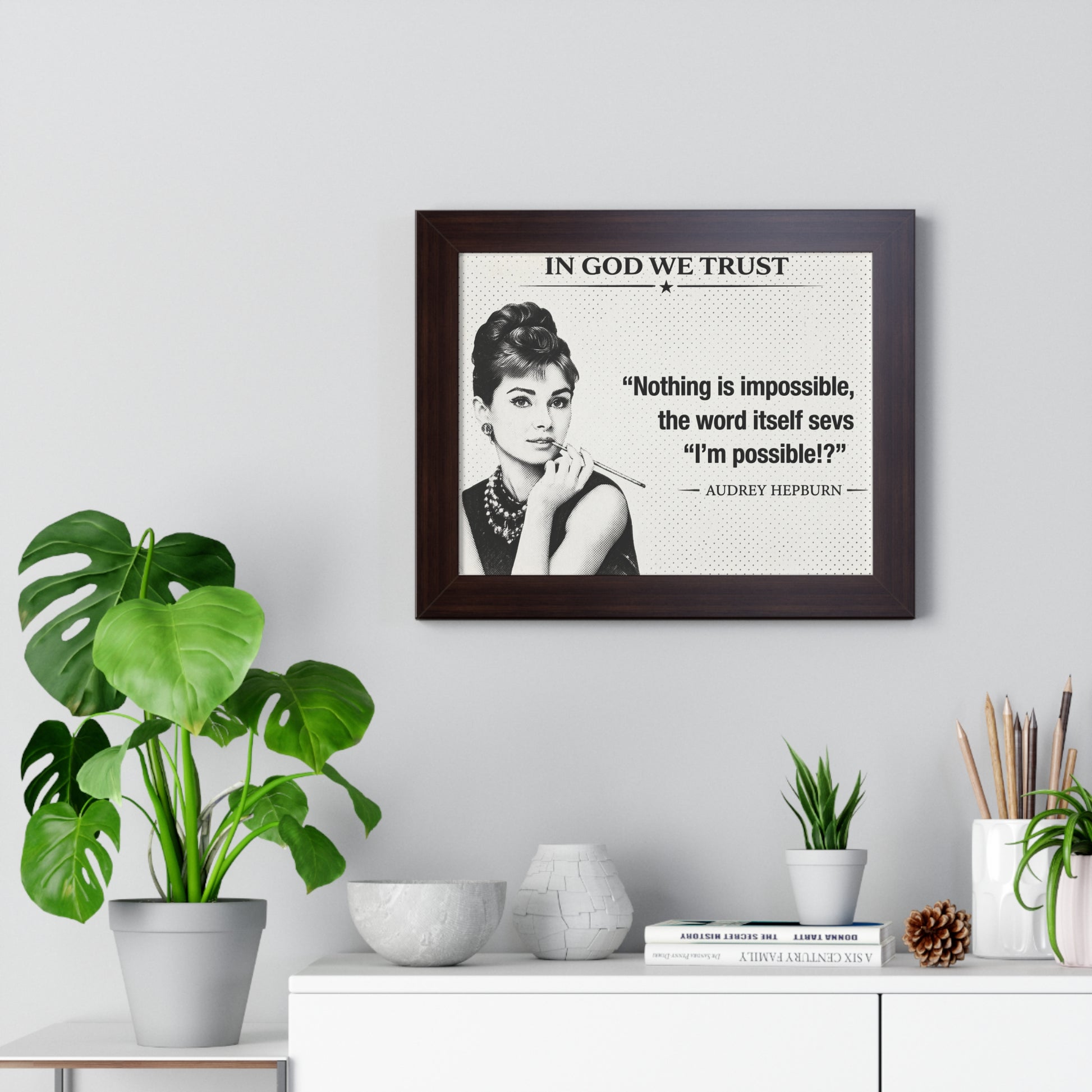 Framed portrait of Audrey Hepburn with a quote on a wall above a desk with plants and decor items.