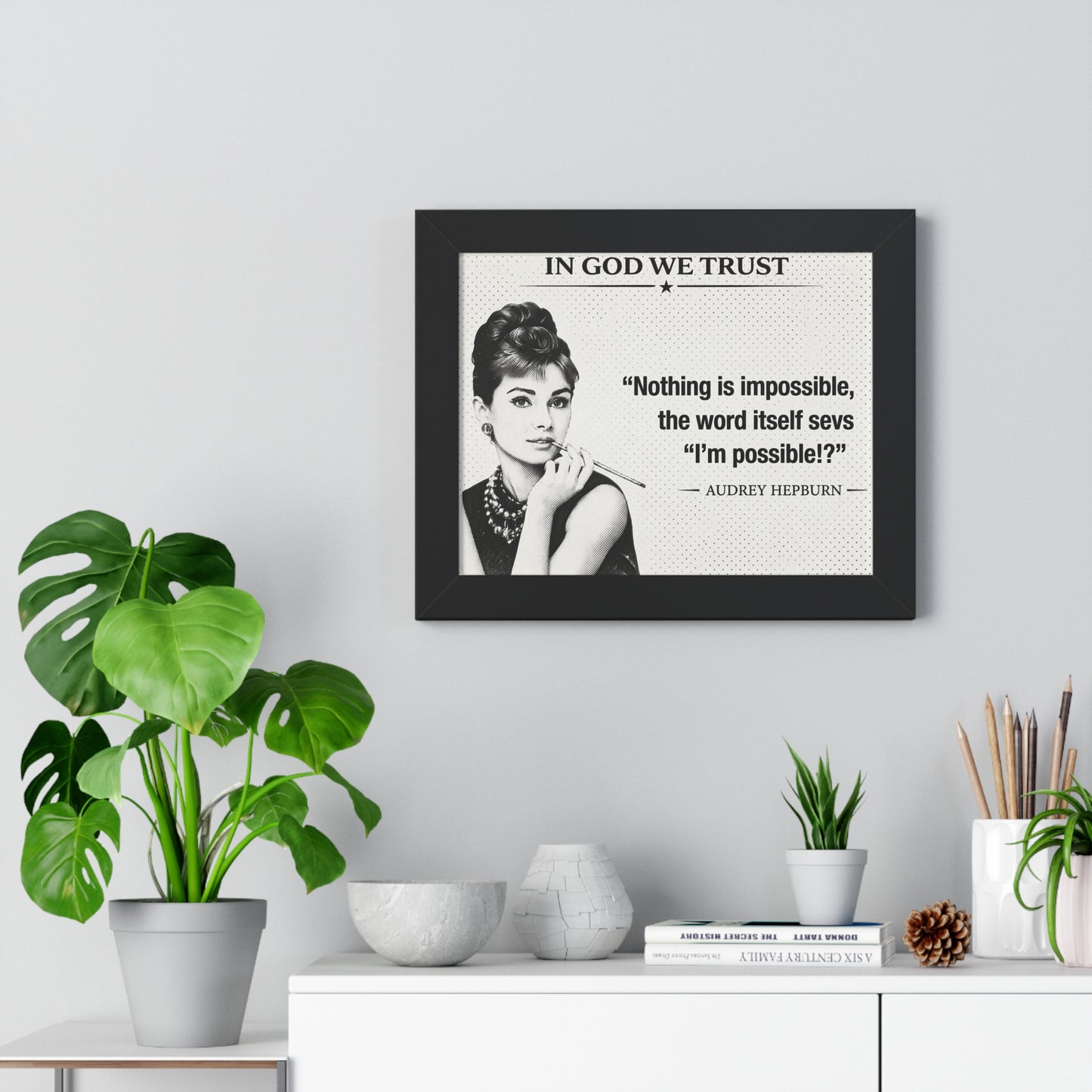 Framed Audrey Hepburn quote on a wall with plants and decor below.
