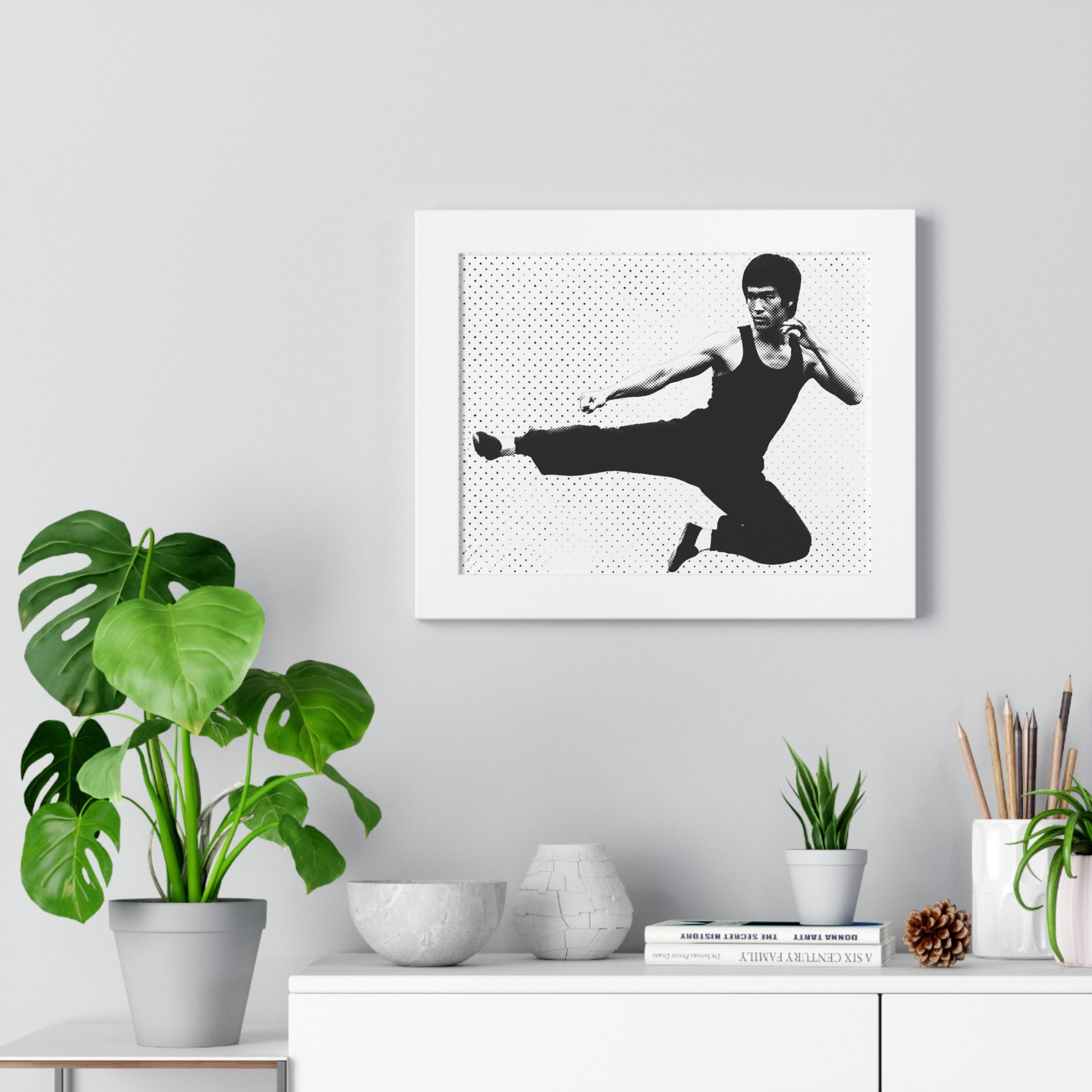 Framed black and white artwork of a martial artist on a wall above a desk with plants and decor.