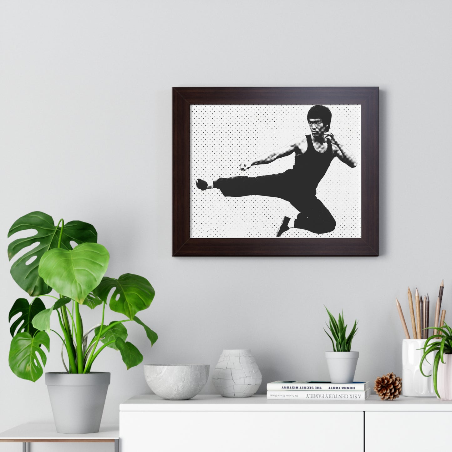 Framed black and white portrait of a martial artist on a wall above a desk with plants and decor.