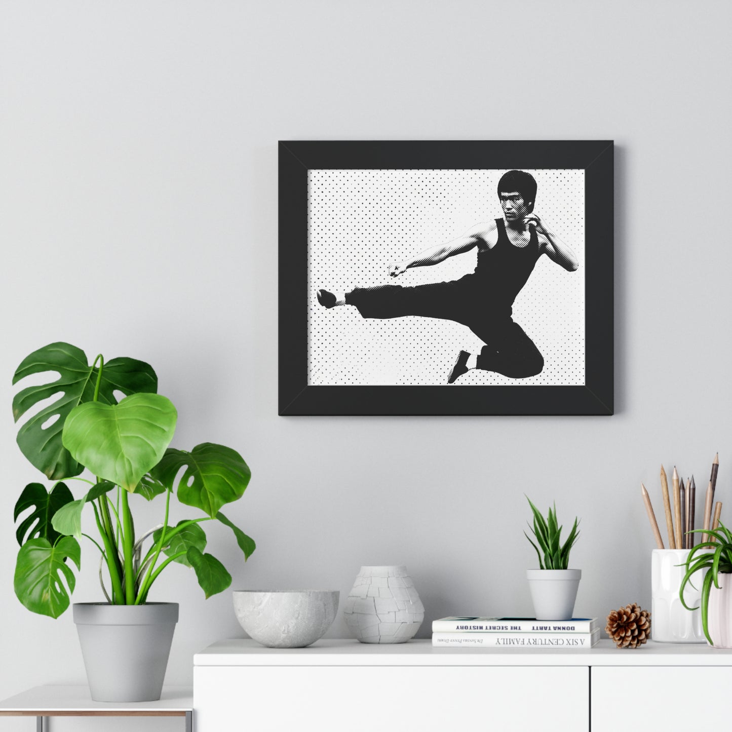 Framed black and white portrait of a martial artist on a wall above a desk with plants and decor.
