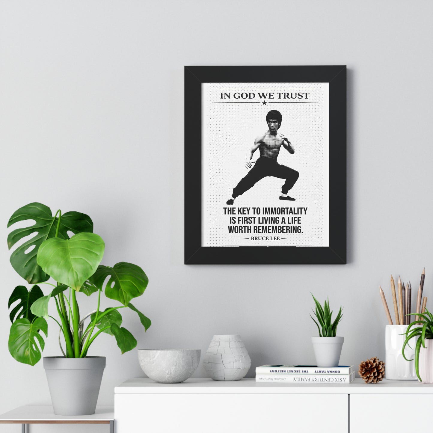 Framed Bruce Lee poster with motivational quote on a wall above a white cabinet with decorative items.