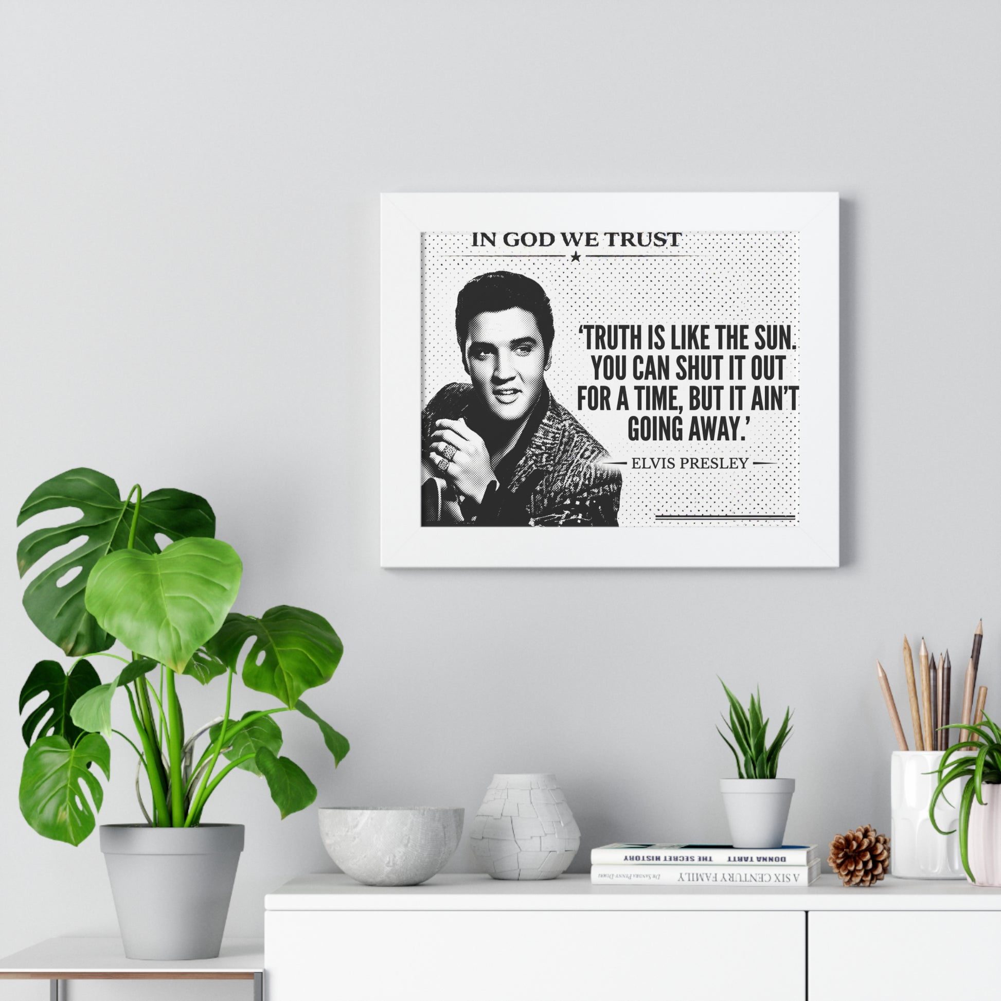 Framed Elvis Presley quote on a wall with plants and decor below.