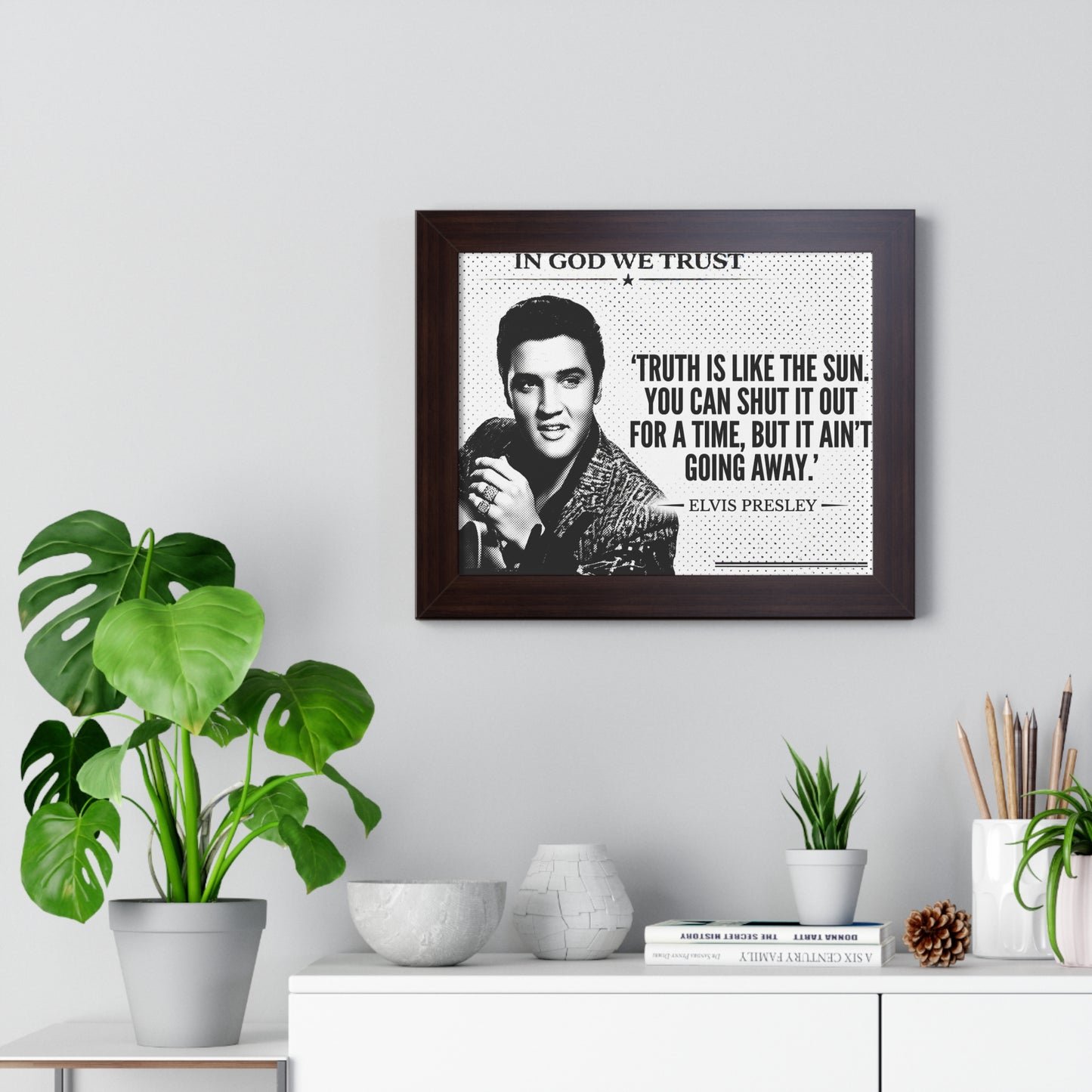 Framed Elvis Presley quote on a wall with plants and decor below.