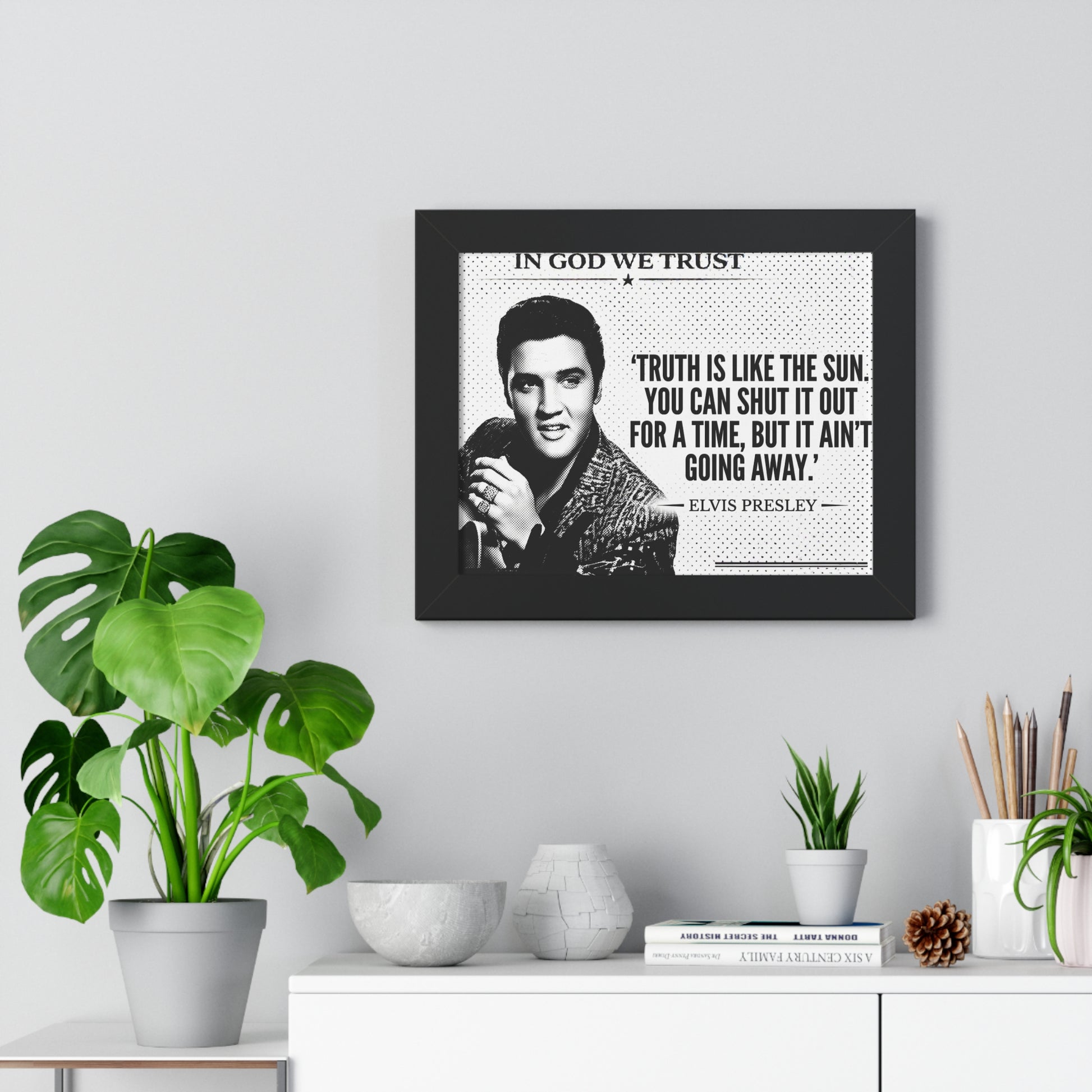 Framed Elvis Presley quote on a wall with plants and decor below.