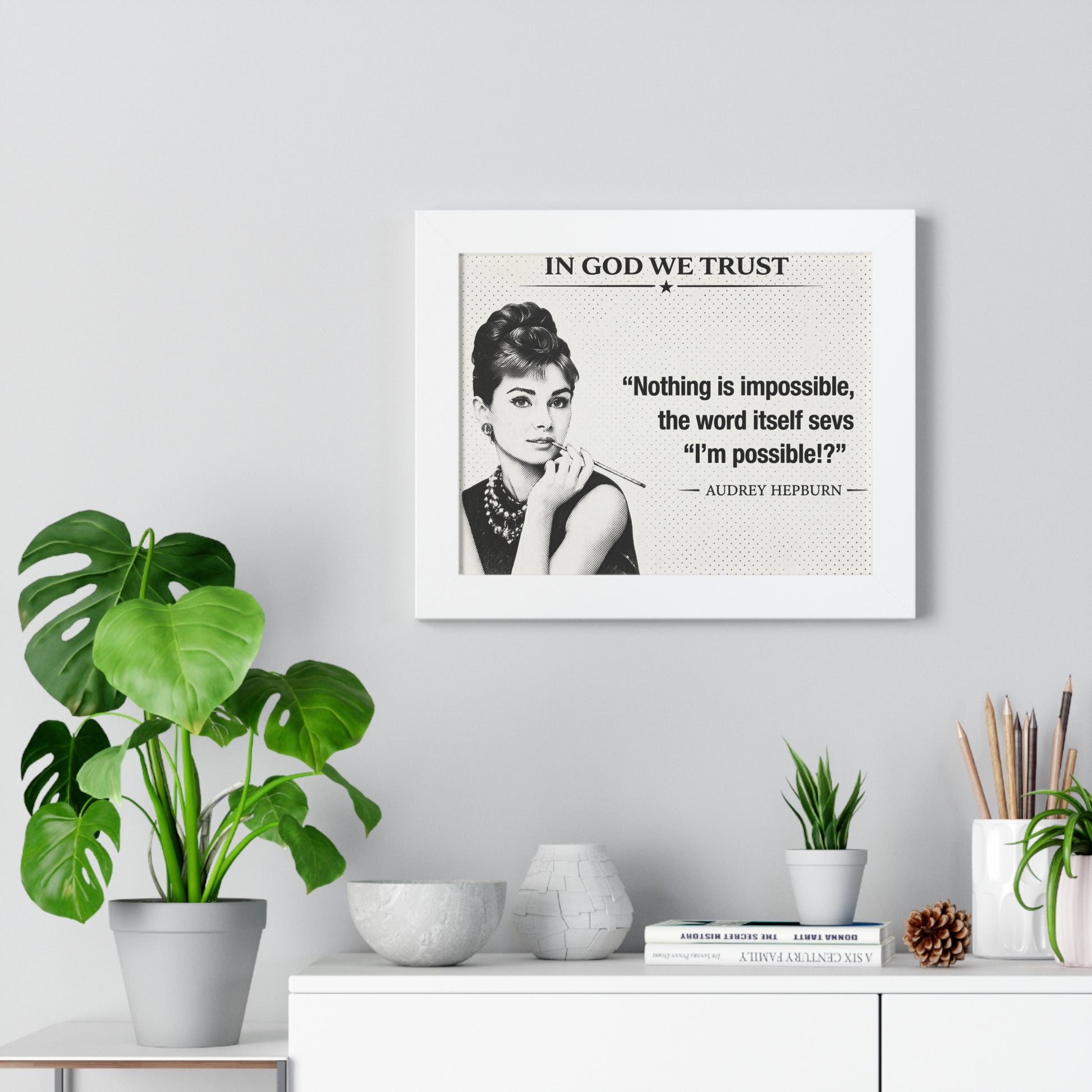 Framed Audrey Hepburn quote on a wall with plants and decor below.