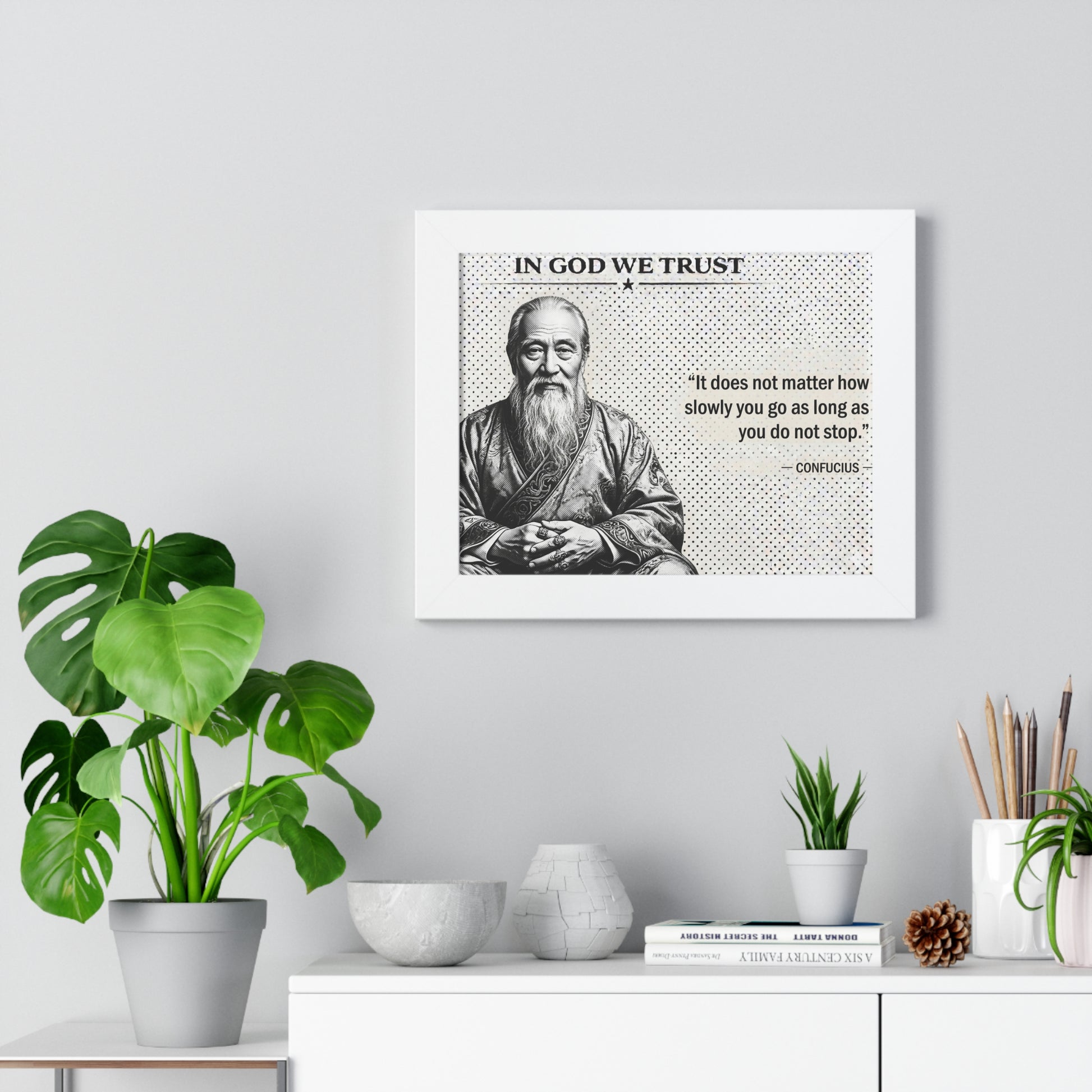 Framed picture of a man with a quote on a wall with plants and decor below.