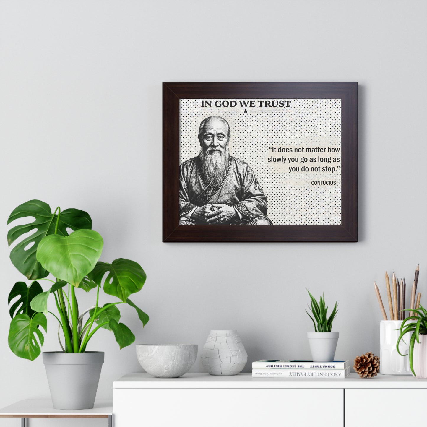 Framed picture of a philosopher with a quote on a wall above a desk with plants and decor.
