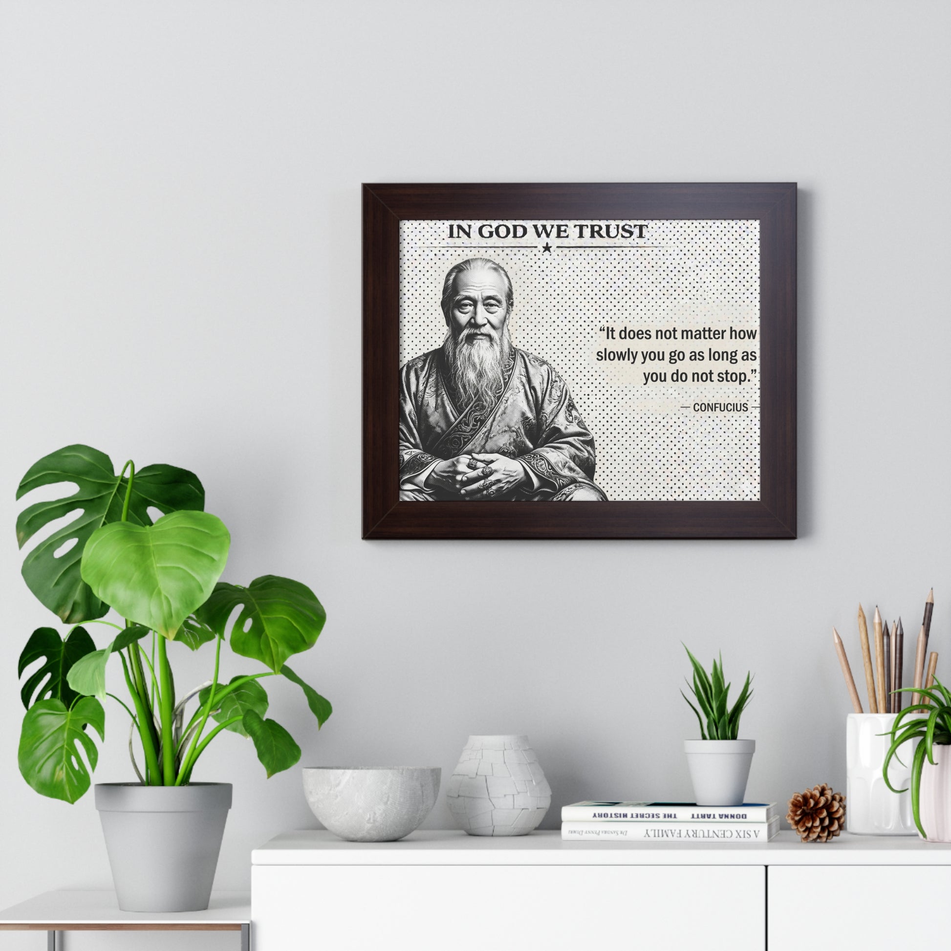 Framed picture of a philosopher with a quote on a wall above a desk with plants and decor.
