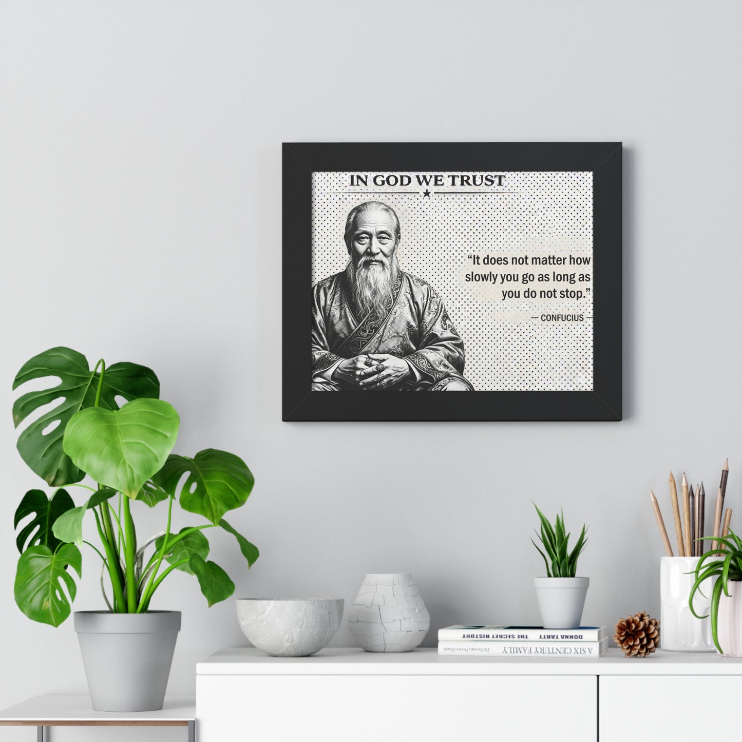 Framed picture of a philosopher with a quote on a wall above a desk with plants and decor.