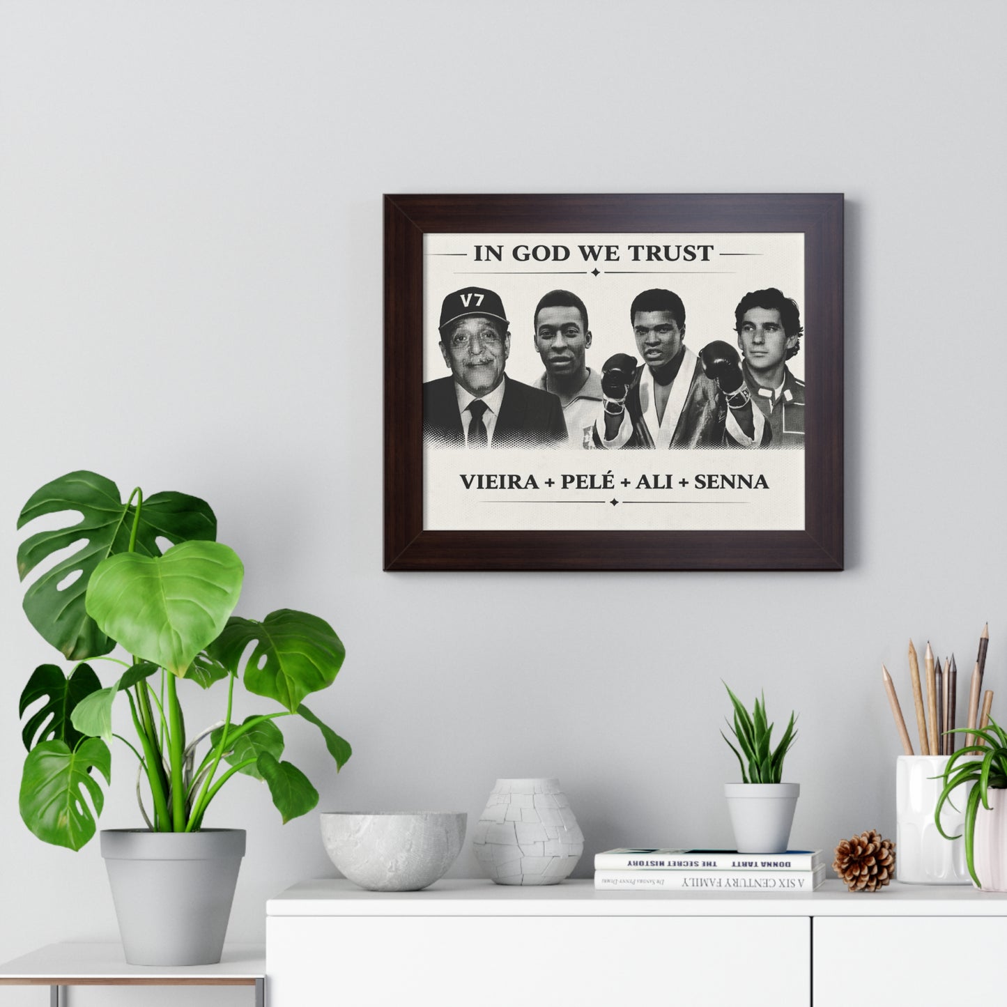 Framed poster with images of famous people and text 'In God We Trust' on a wall with decorative items below.