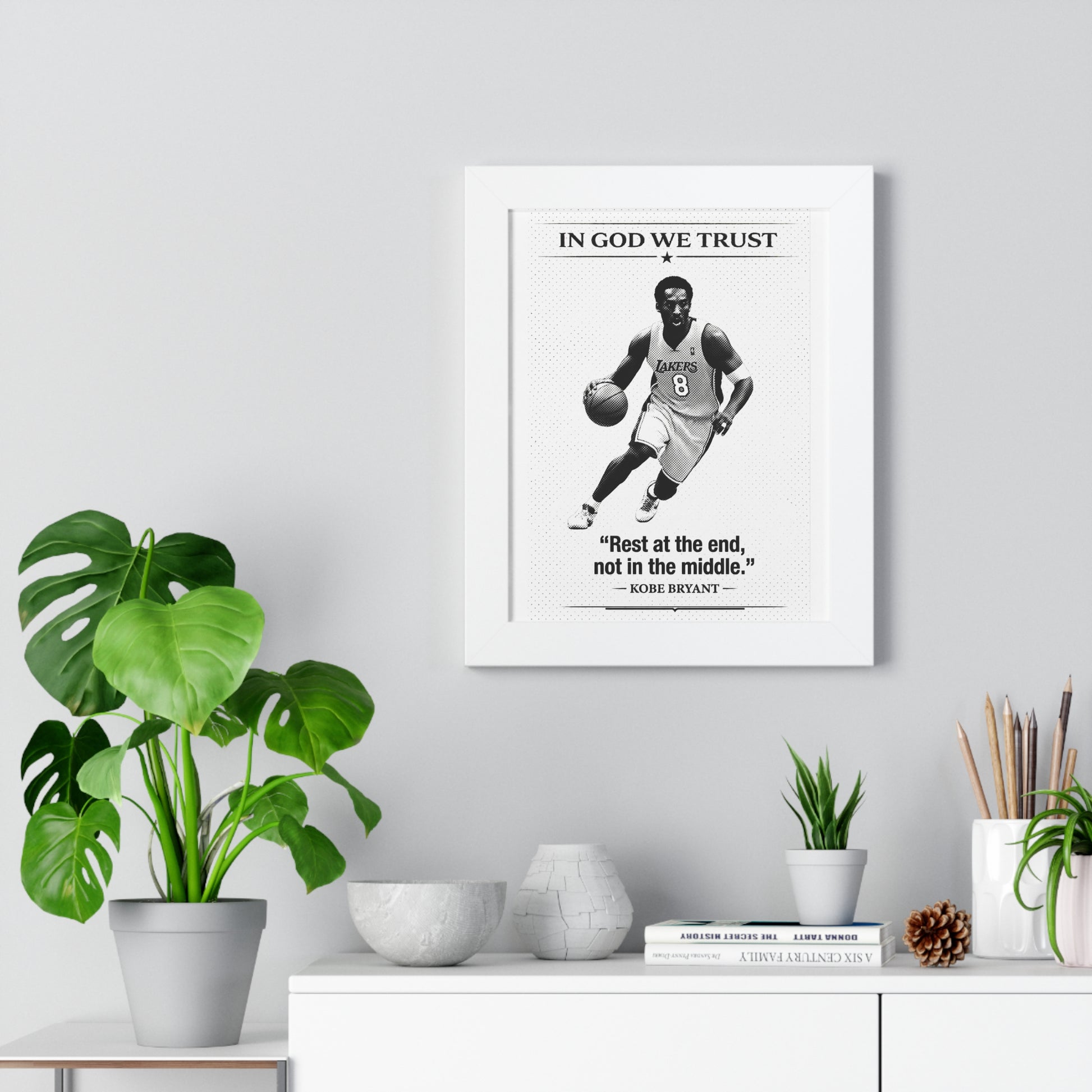 Framed artwork of a basketball player with a quote on a wall above a desk with plants and decor.