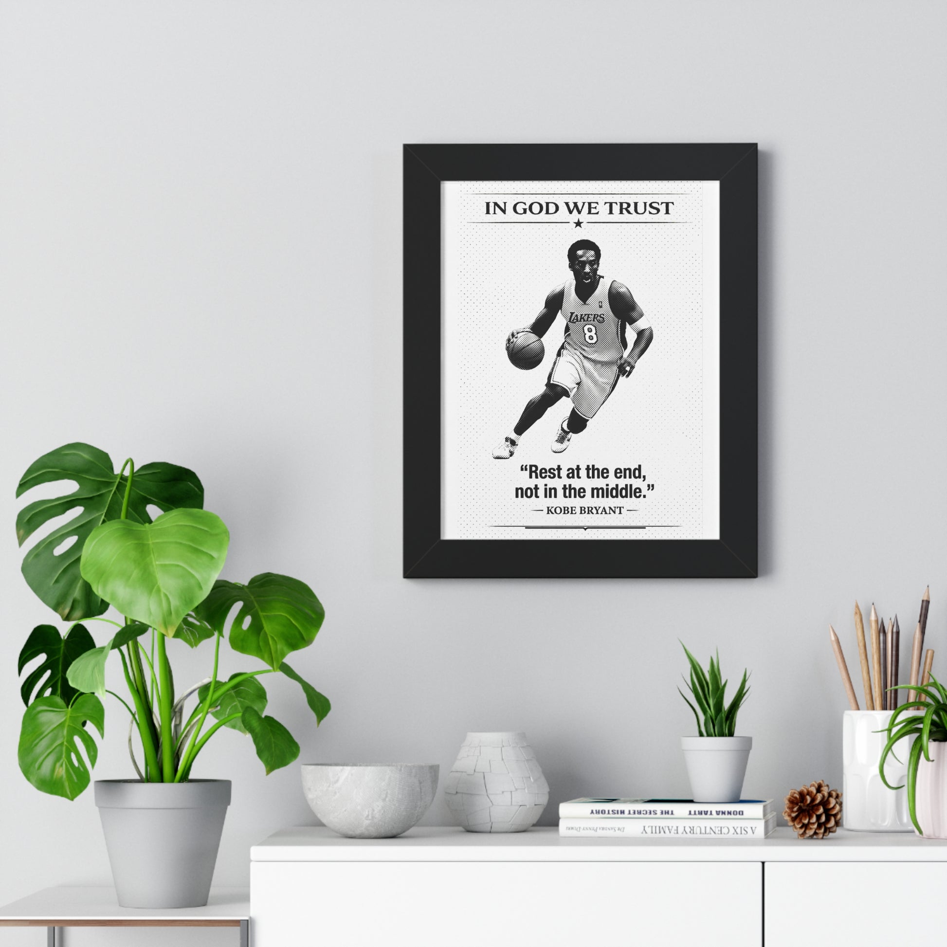 Framed poster with a basketball player and quote on a wall above a desk with plants and decor.