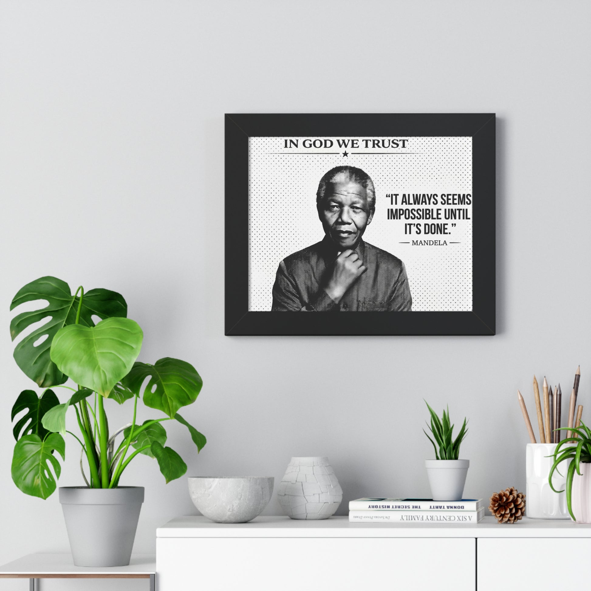 Framed poster with a quote and portrait of a famous person, placed on a wall above a white cabinet with decorative items.