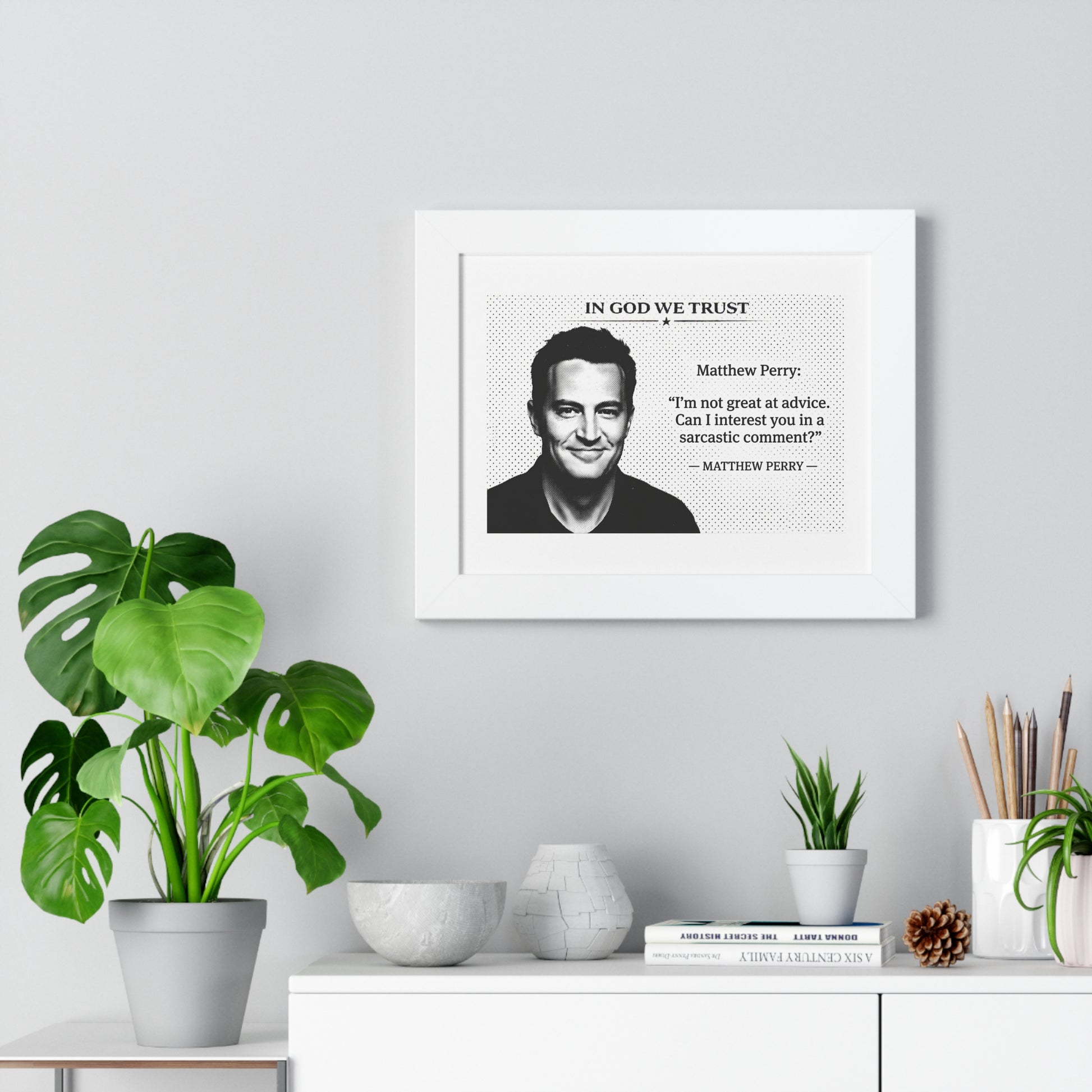 Framed artwork with a quote by Matthew Perry on a wall above a desk with plants.