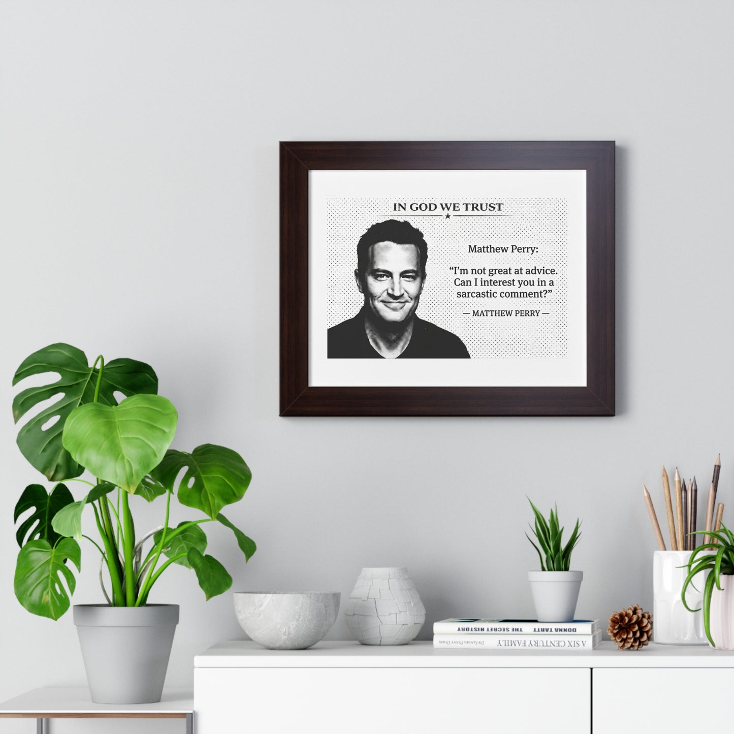 Framed print with a quote by Matthew Perry on a wall above a desk with plants and decor items.