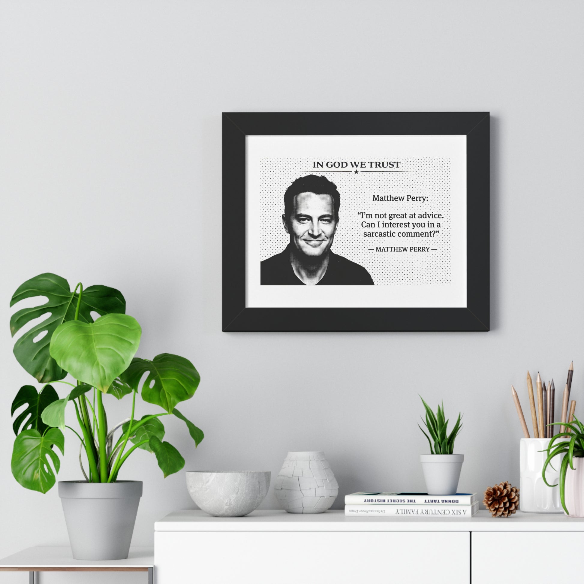 Framed print with a quote by Matthew Perry on a wall above a white cabinet with decorative items.