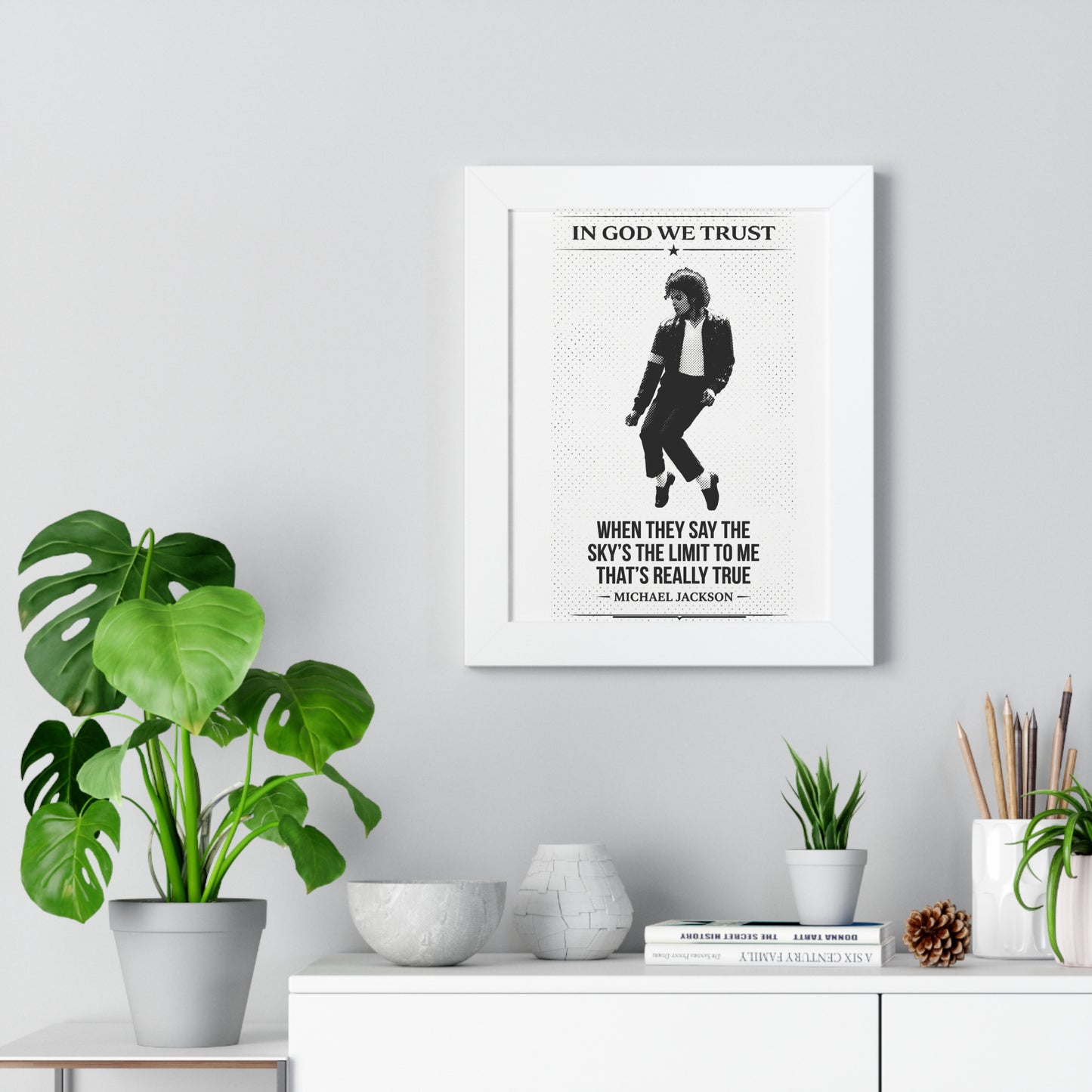 Framed poster with a silhouette of a person and text on a wall above a white cabinet with decorative items.