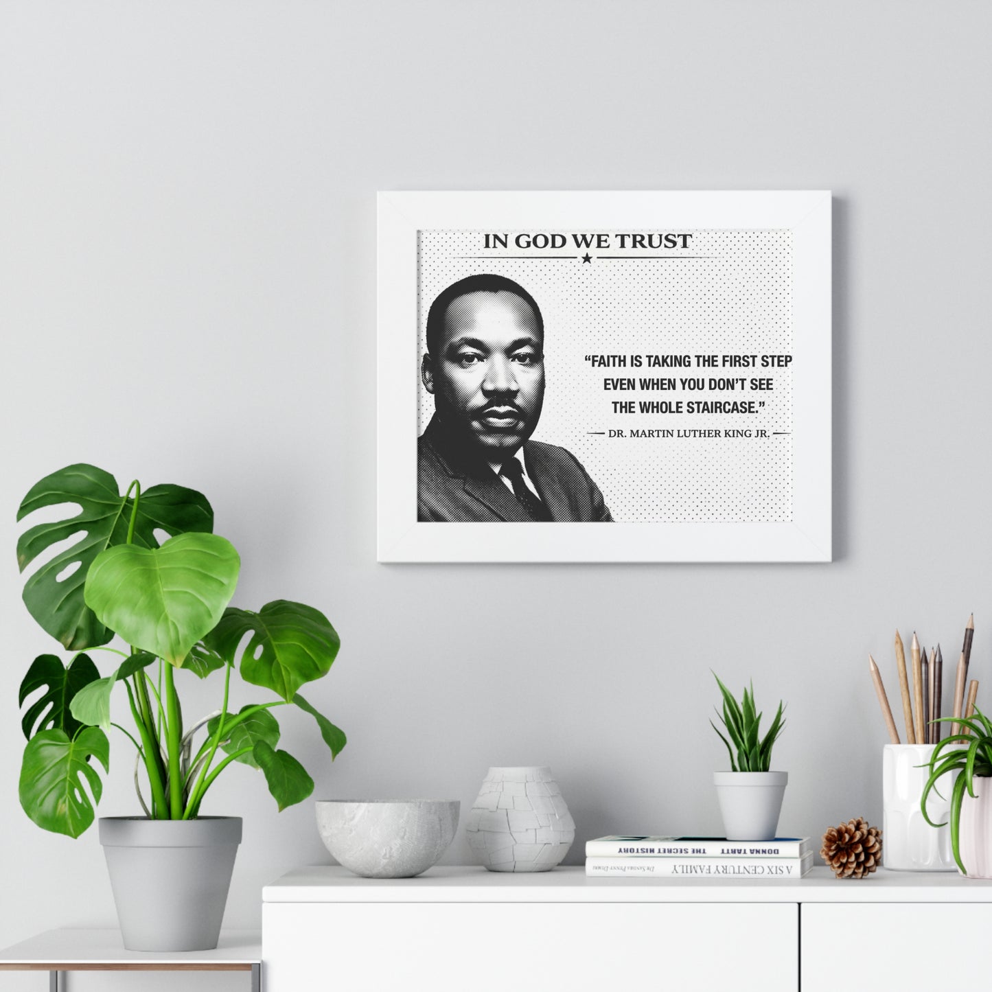 Framed portrait of a historical figure with a quote on a wall above a desk with plants and decor.