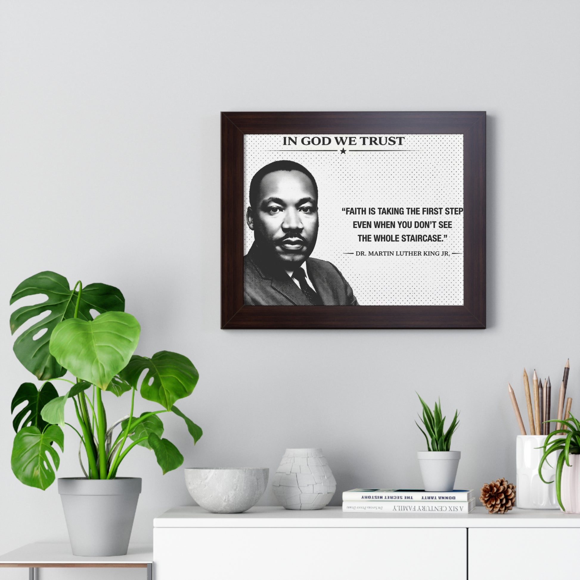 Framed portrait of a historical figure with a quote on a wall above a desk with plants and decor.