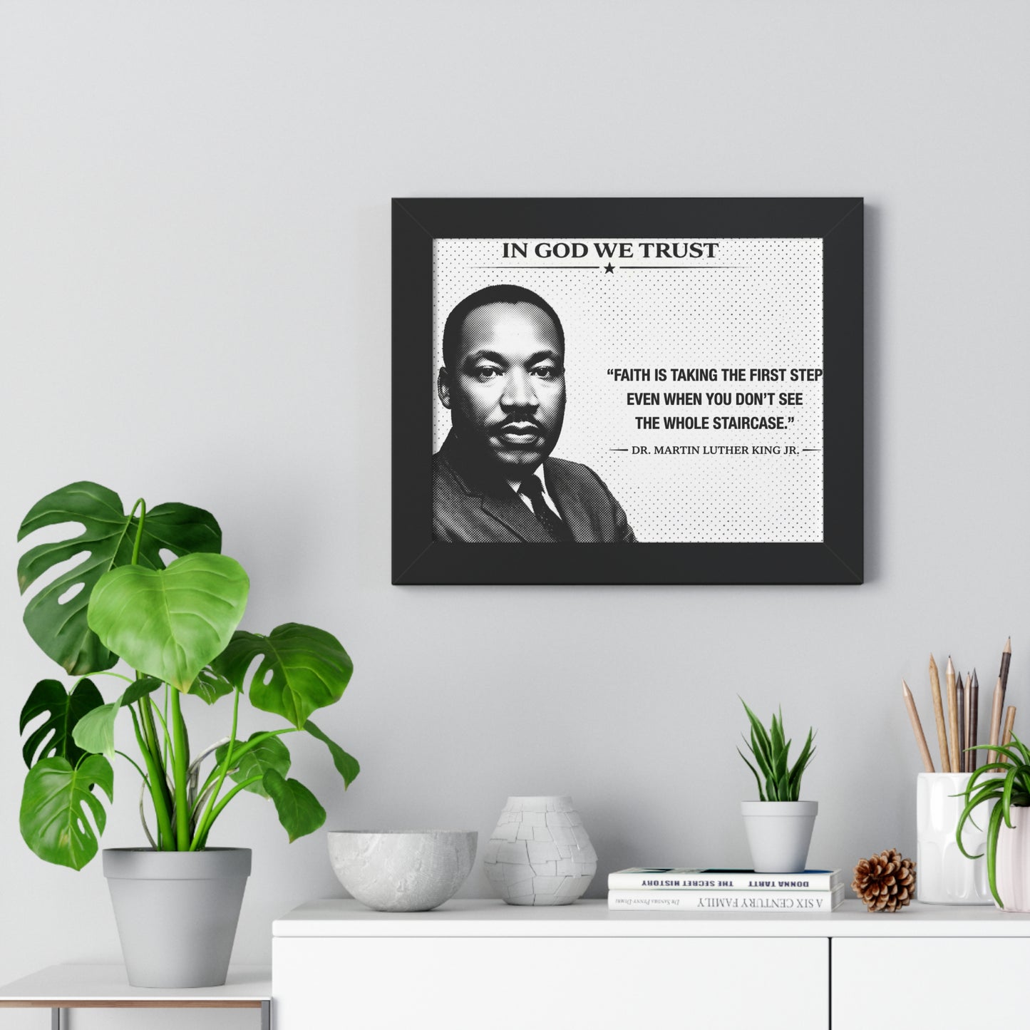 Framed portrait of a historical figure with a quote on a wall above a white cabinet with decorative items.