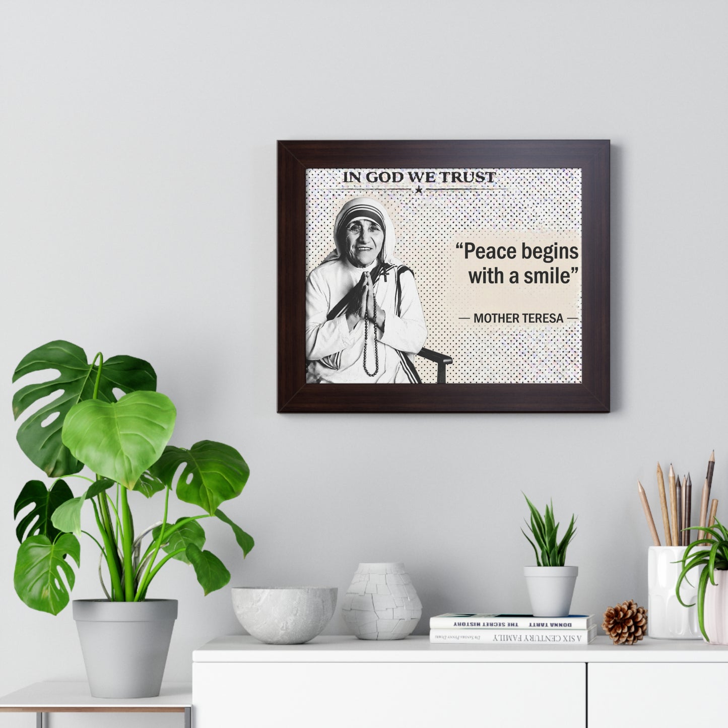 Framed quote by Mother Teresa on a wall with decorative plants and items.