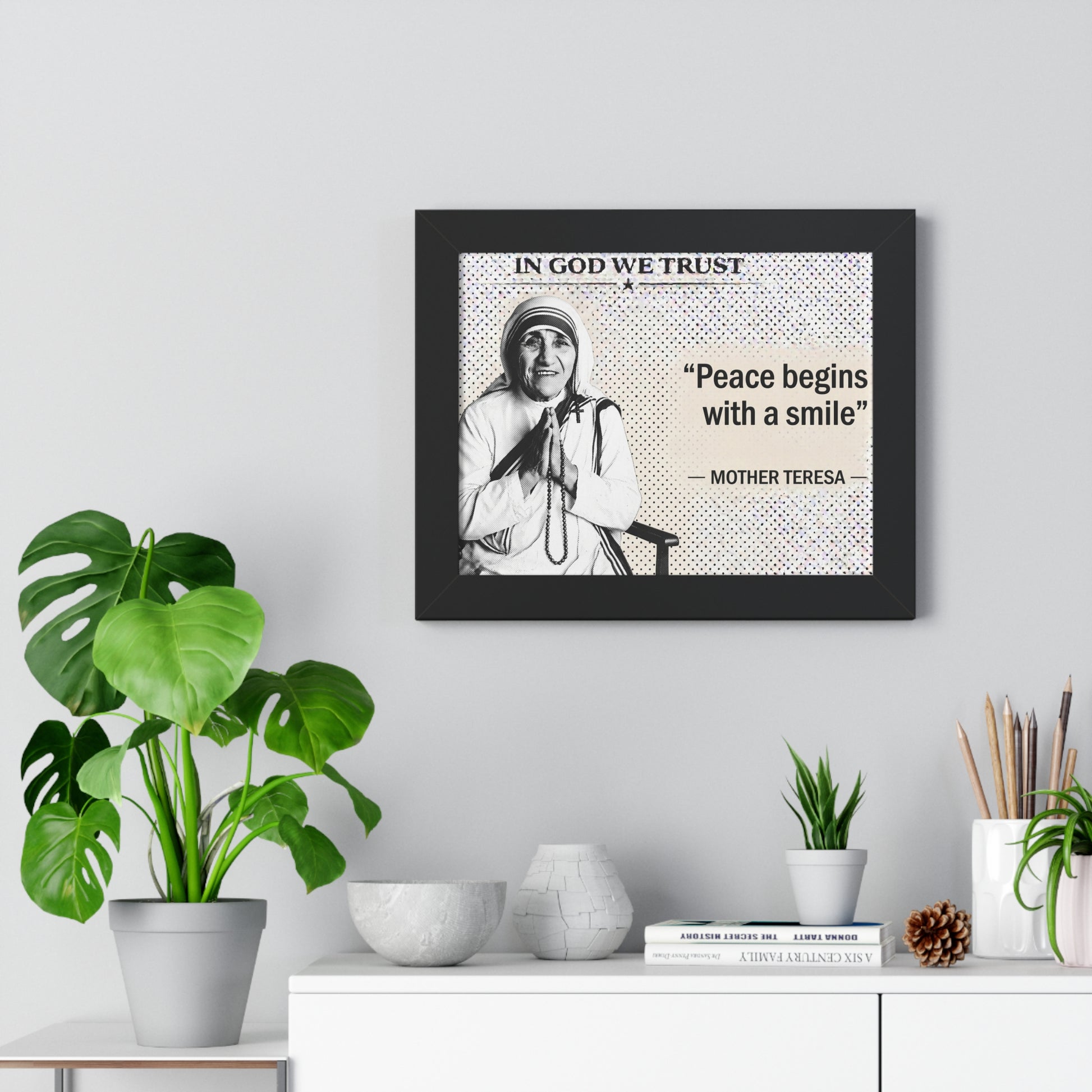 Framed picture of Mother Teresa with a quote on a wall above a white cabinet with decorative items.