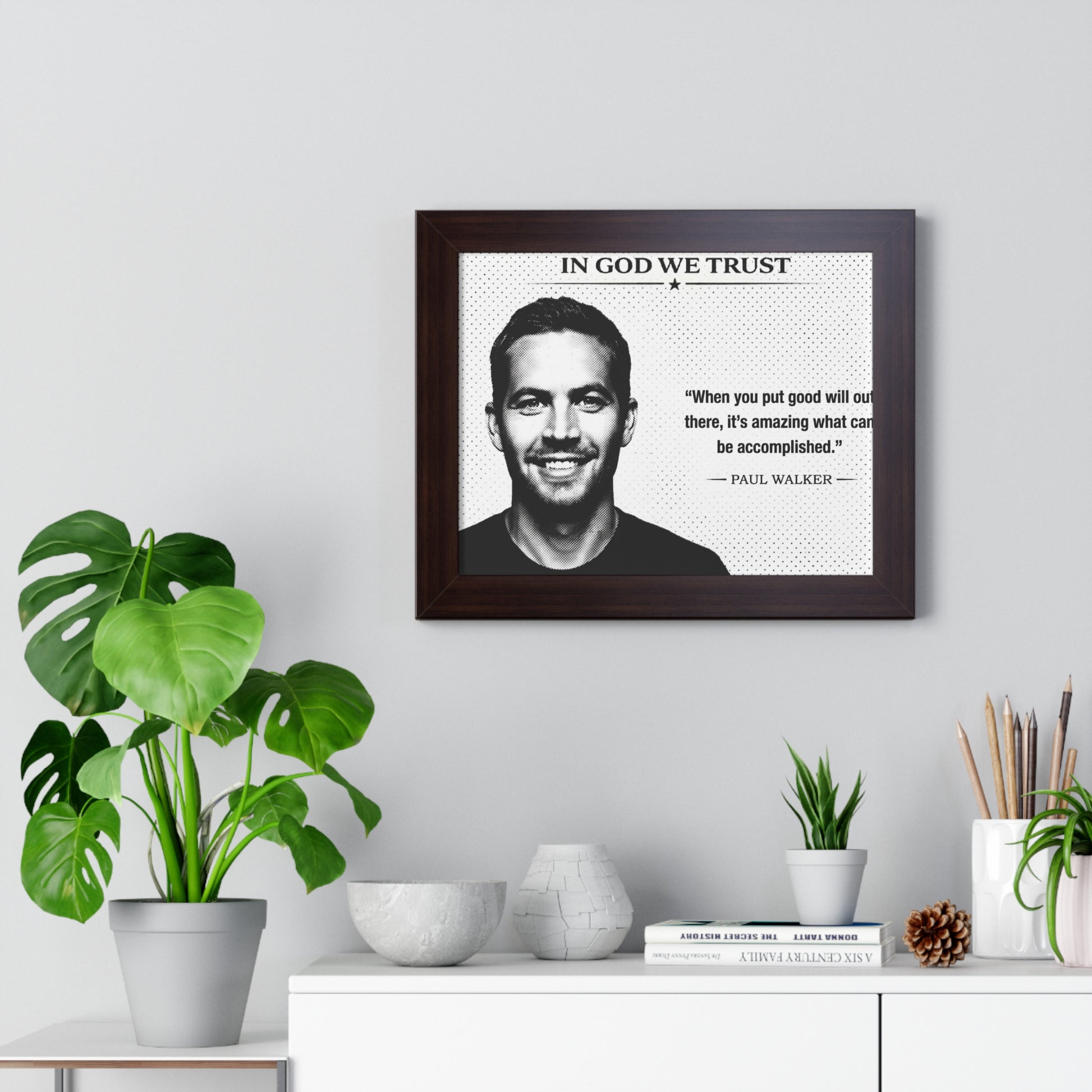 Framed portrait of a man with a quote on a wall above a white cabinet with decorative items.