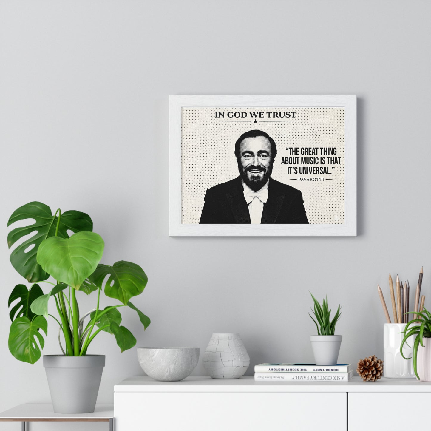 Framed poster with a quote and portrait of a man on a wall above a white cabinet with decorative items.