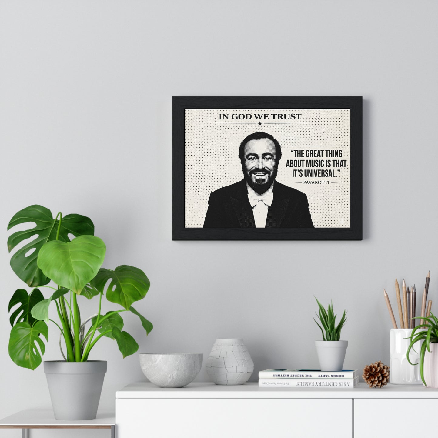 Framed picture of a man with a quote on a wall above a white cabinet with decorative items.