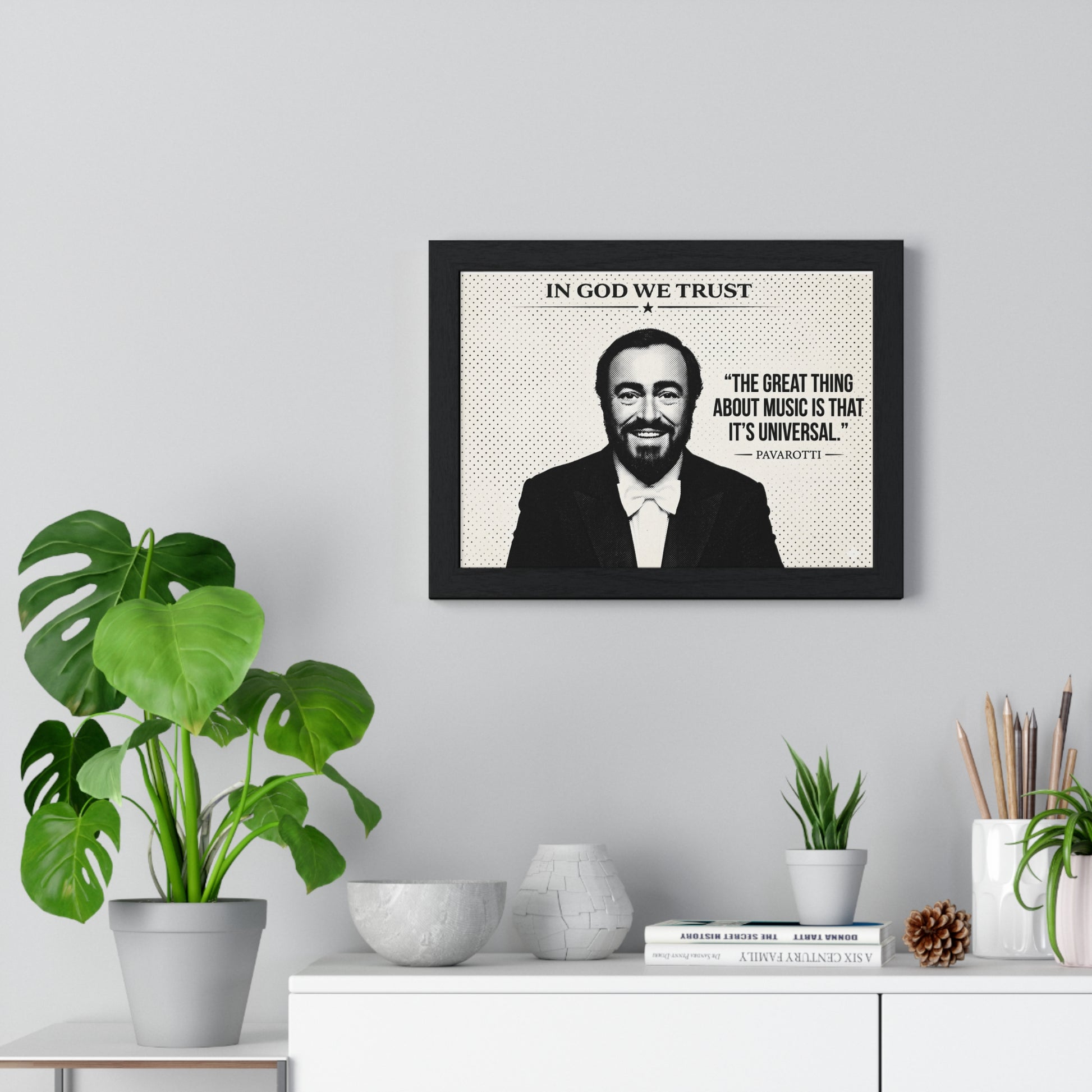 Framed picture of a man with a quote on a wall above a white cabinet with decorative items.