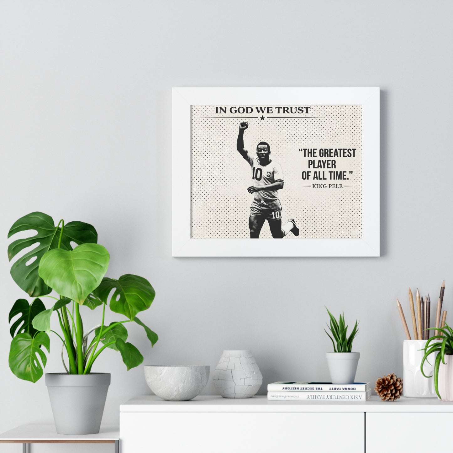 Framed artwork with a sports player and text on a wall above a white cabinet with decorative items.