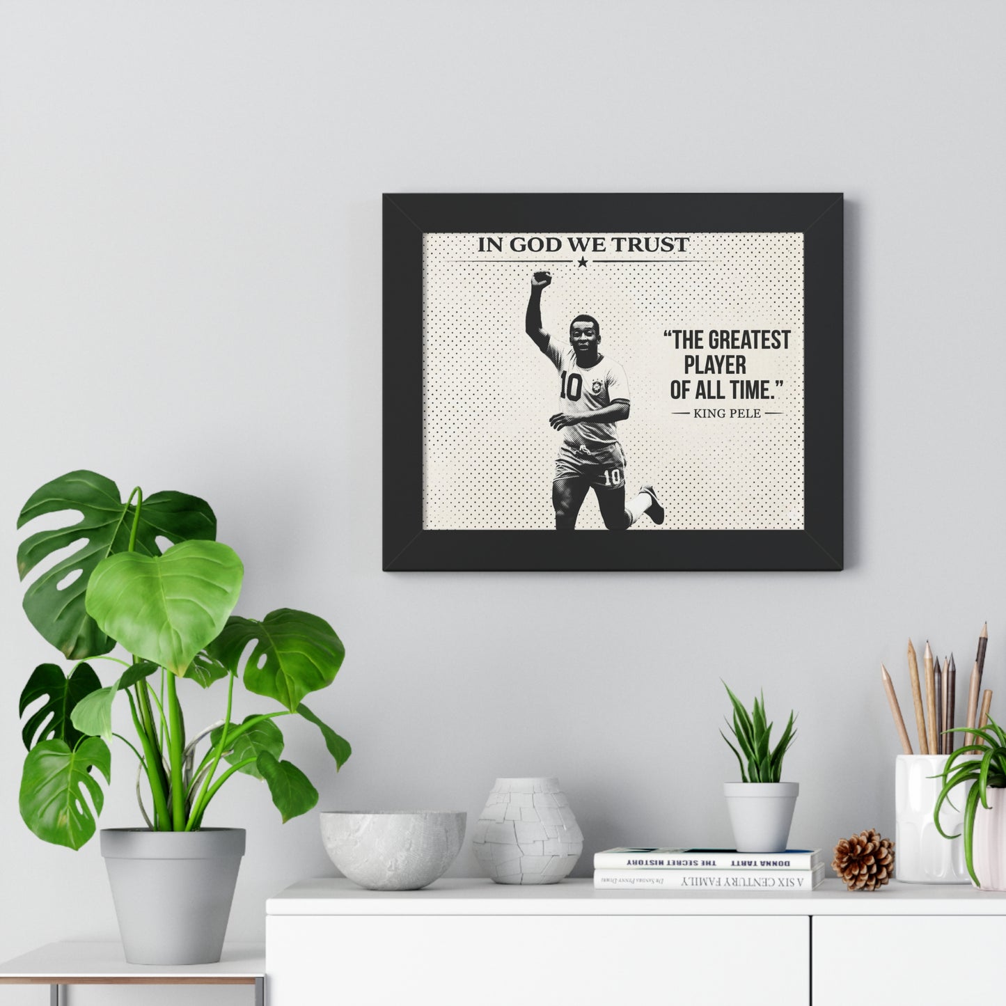 Framed poster with a sports player and text on a wall above a white cabinet with decorative items.