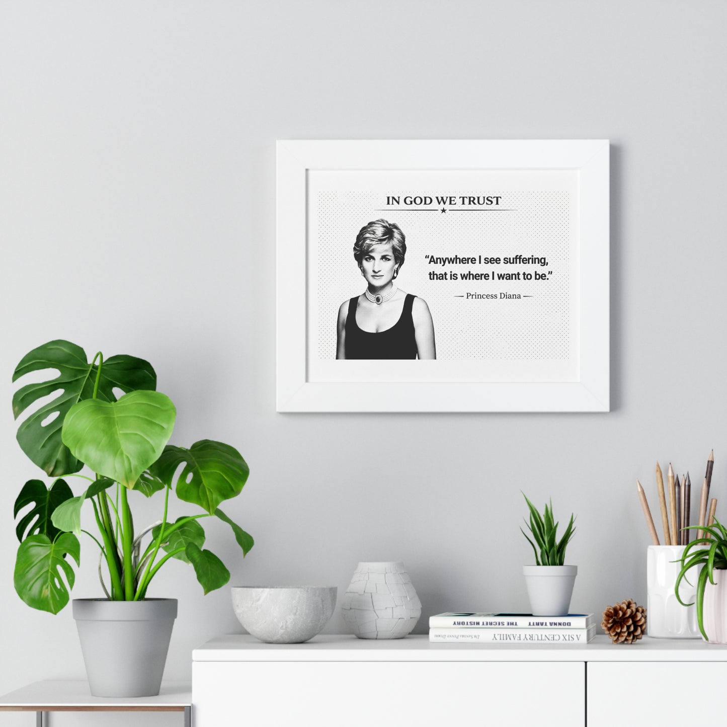 Framed quote print on a wall with decorative plants and books below.