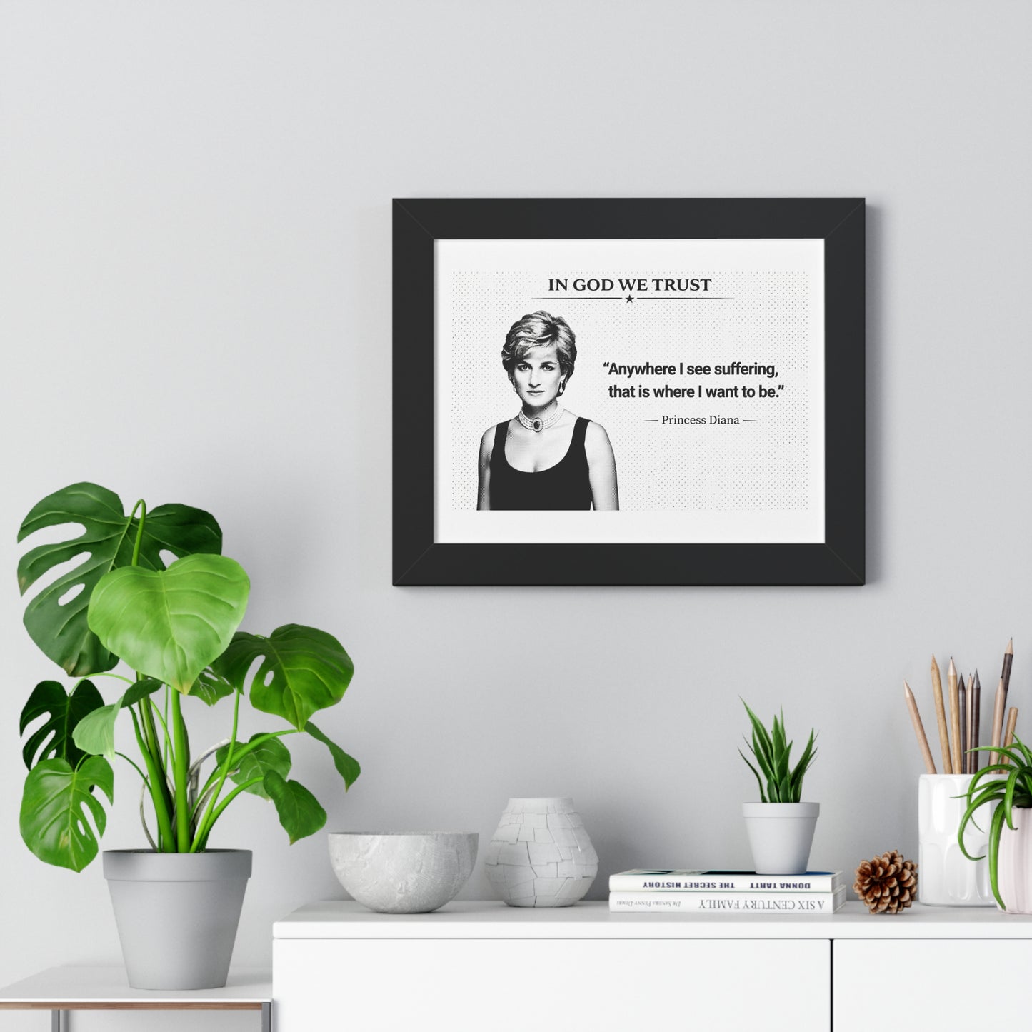 Framed picture of Princess Diana with a quote on a wall above a white cabinet with decorative items.