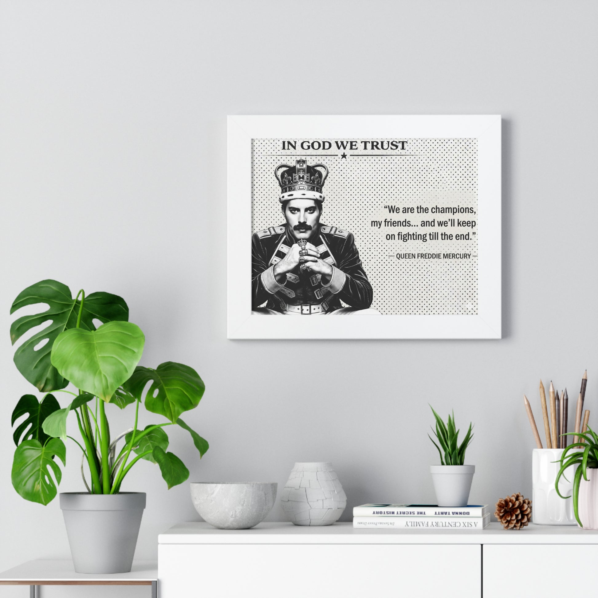 Framed poster with Freddie Mercury quote on a wall with plants and decor below.