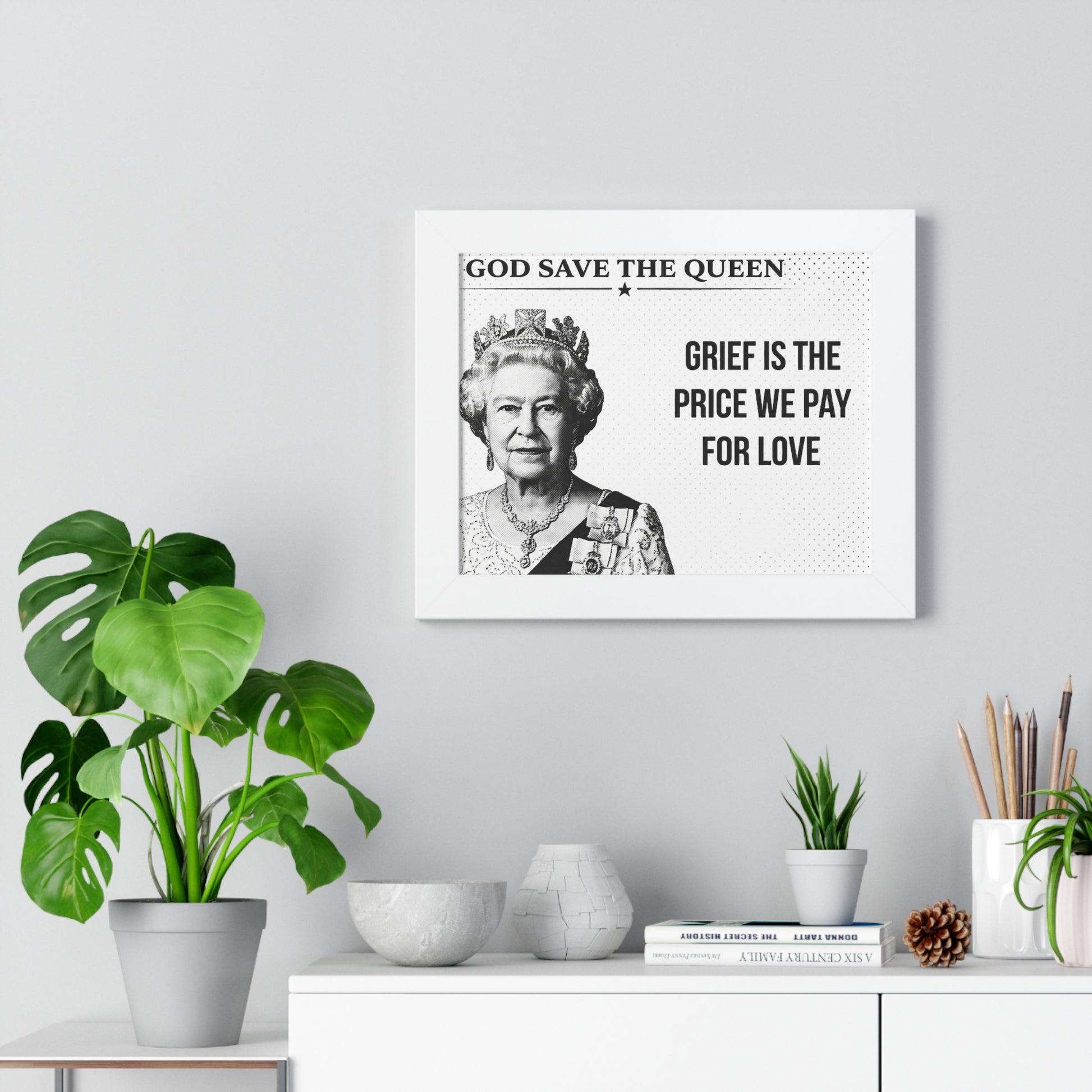 Framed portrait of a monarch with text on a wall above a white cabinet with decorative items.