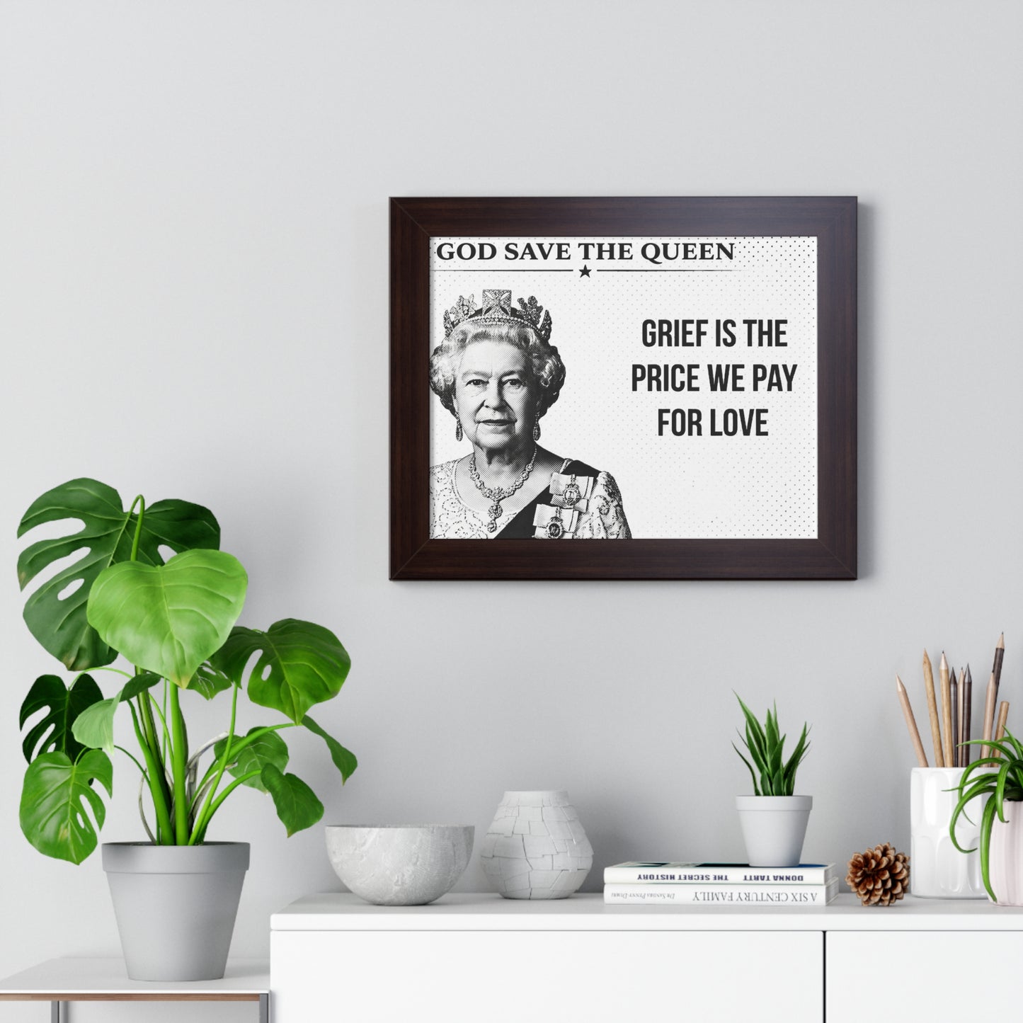 Framed portrait of a monarch with text on a wall above a white cabinet with decorative items.