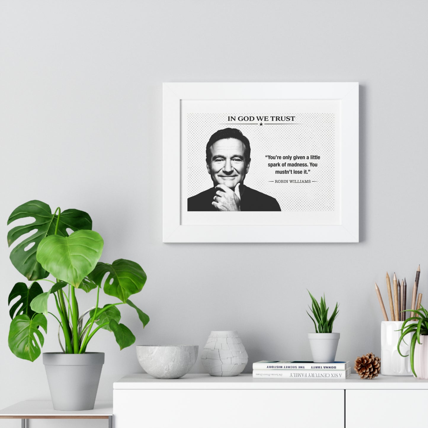 Framed print with a quote on a wall above a desk with plants and decor items.