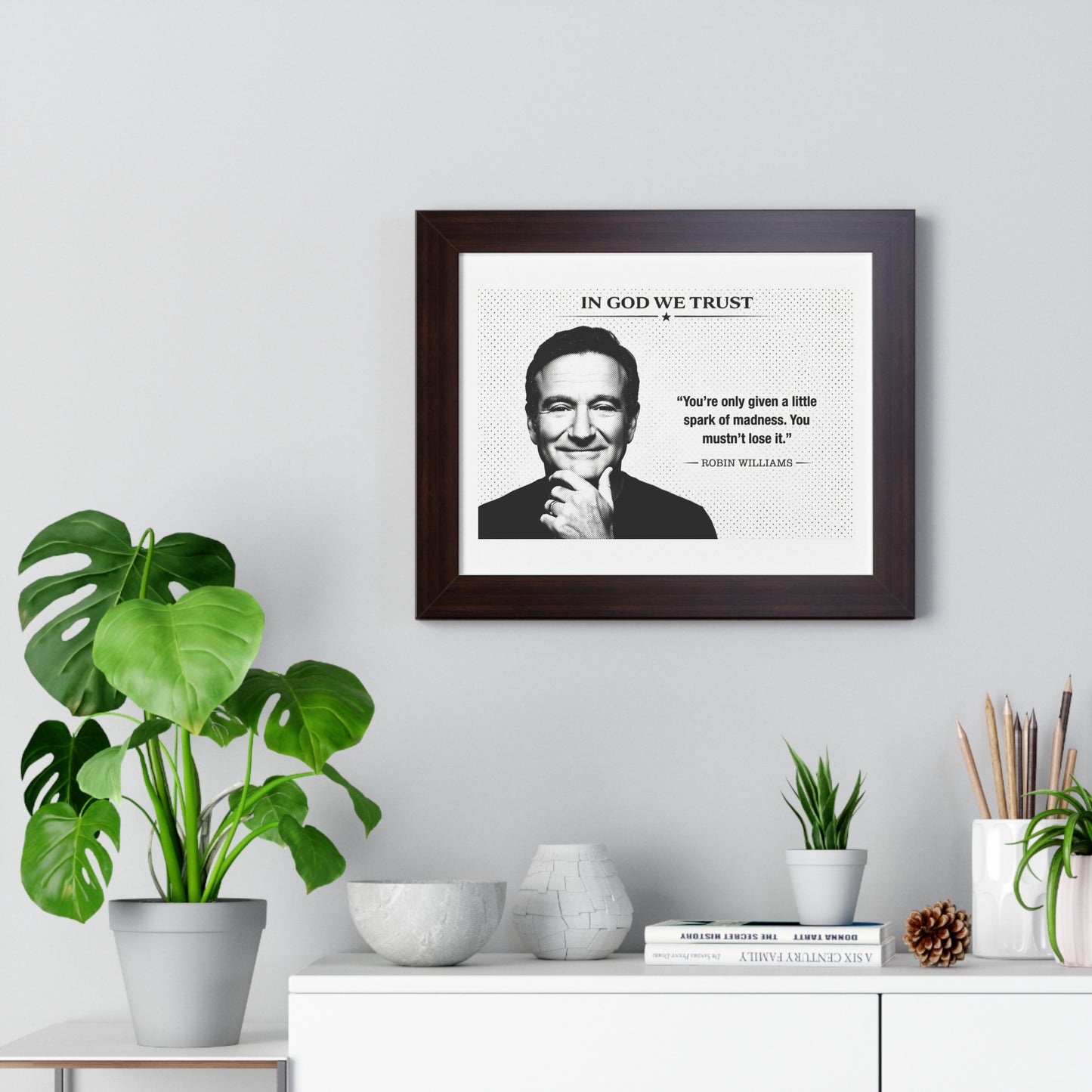 Framed picture of a man with text on a wall above a white cabinet with decorative items.