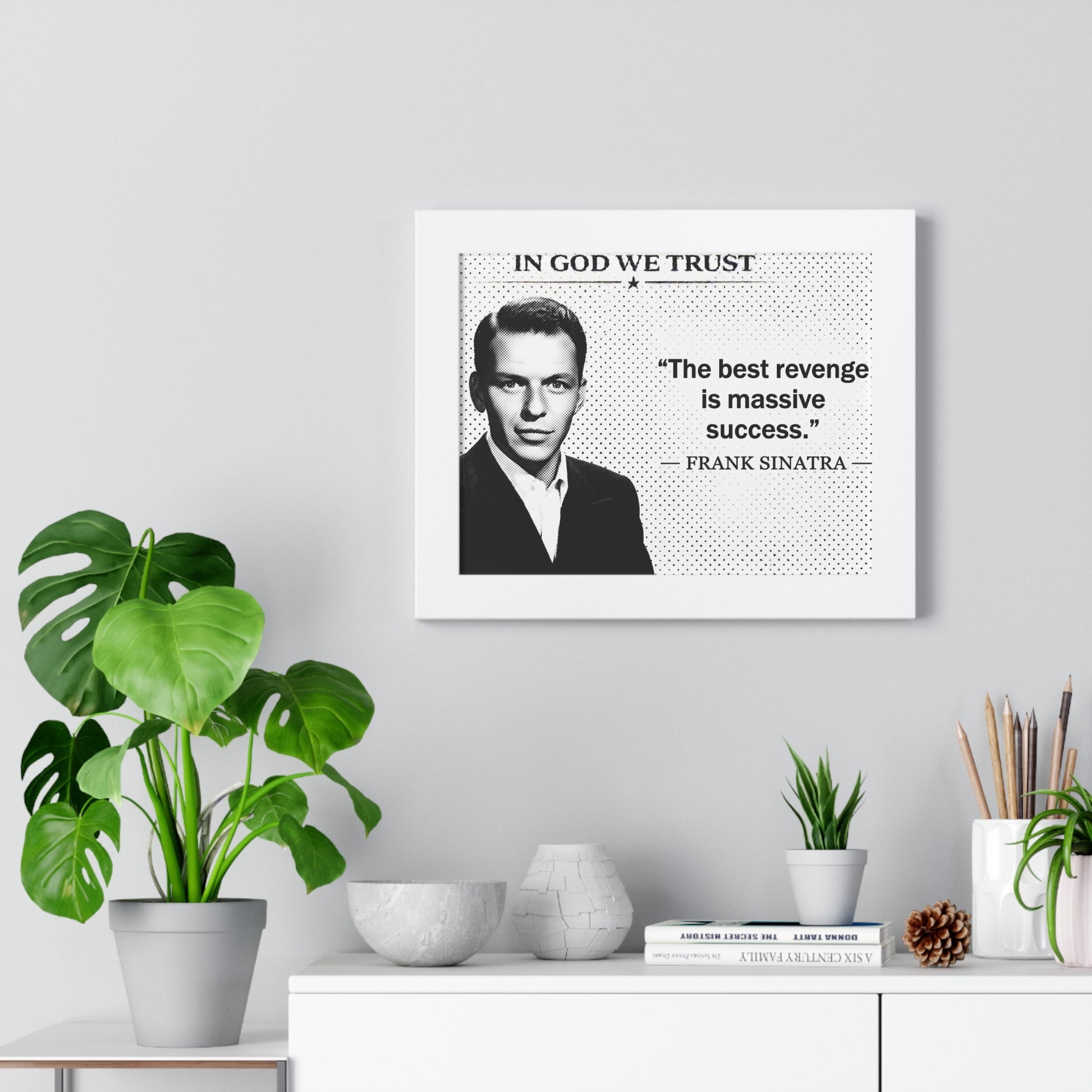 Framed portrait of a man with a quote on a wall above a desk with plants and decor items.