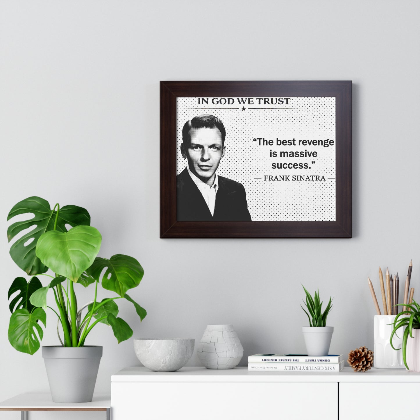 Framed portrait of a man with a quote on a wall above a desk with plants and decor.