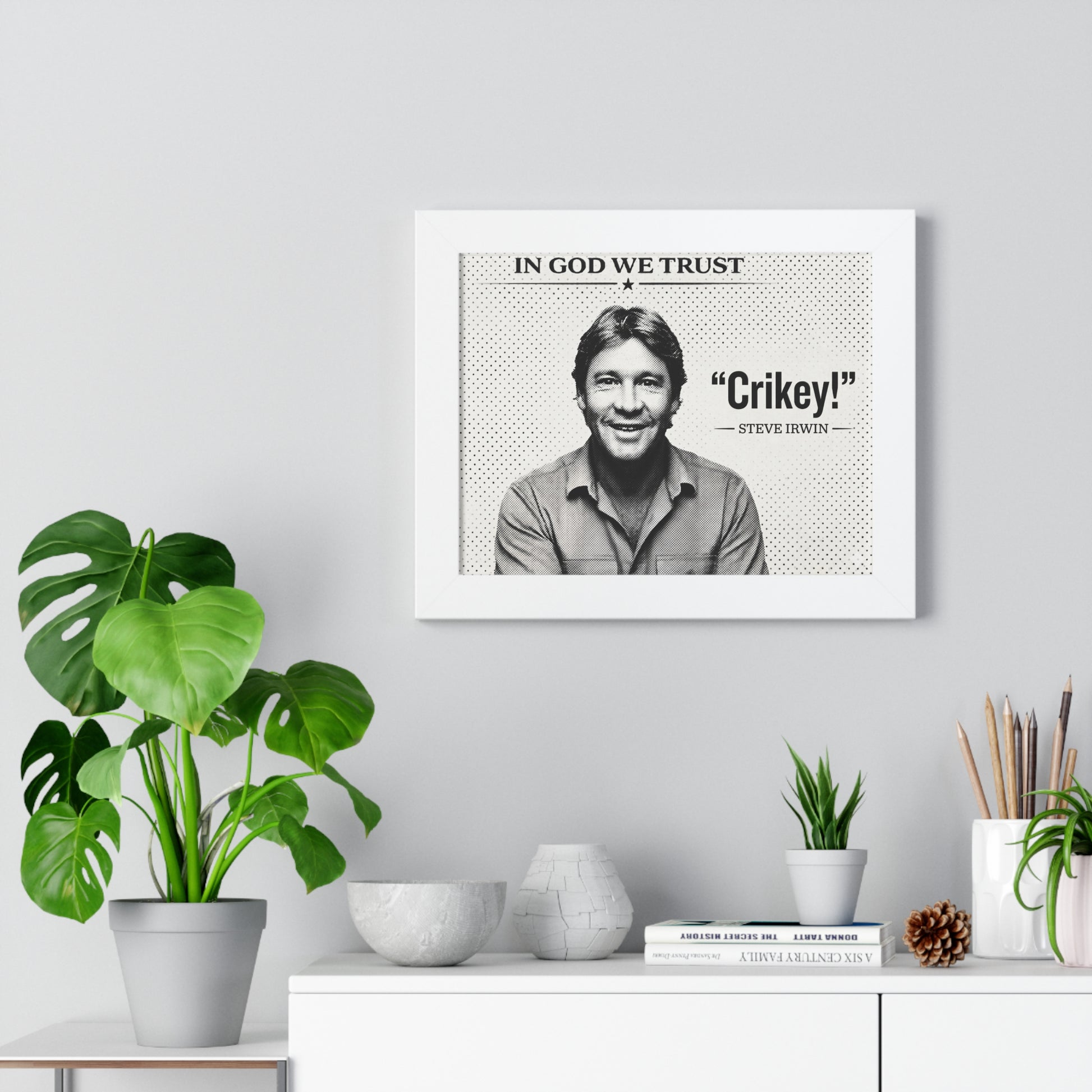 Framed artwork with a portrait and text on a wall above a white cabinet with decorative items.