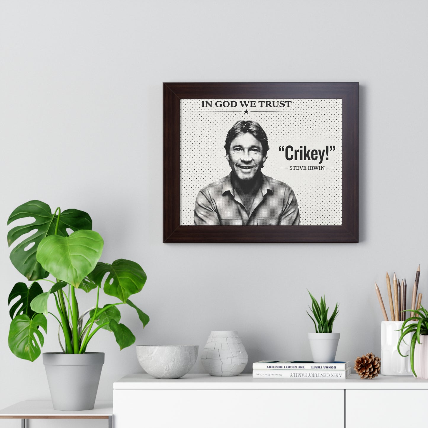 Framed print with a quote by Steve Irwin on a wall above a desk with plants and decor items.