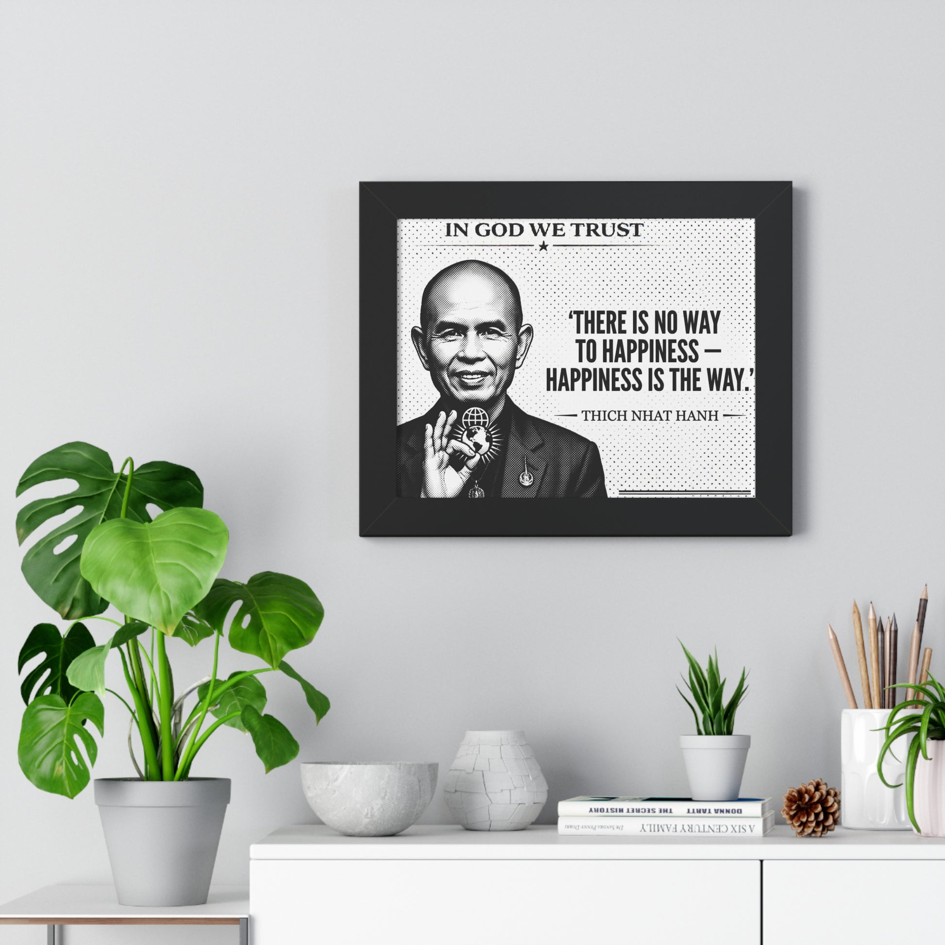 Framed picture of a man with a quote on a wall above a white cabinet with plants.