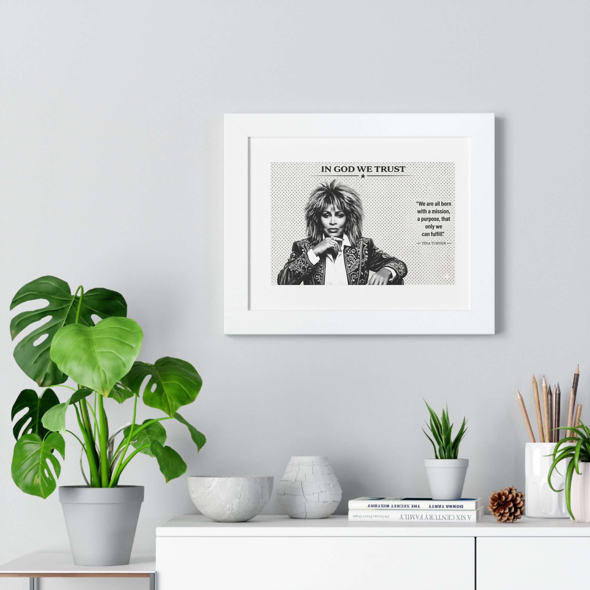 Framed artwork on a wall with decorative plants and items below.