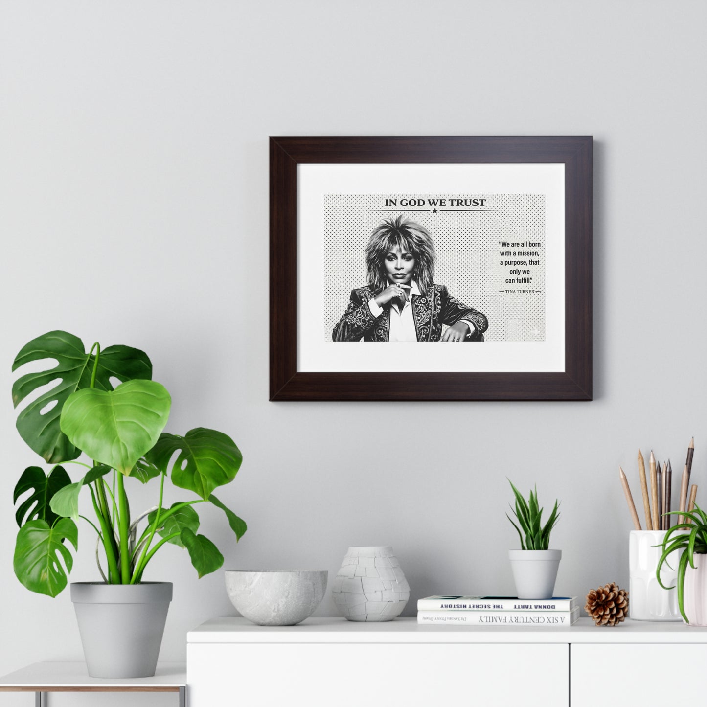 Framed artwork with a quote on a wall above a white cabinet with decorative items.