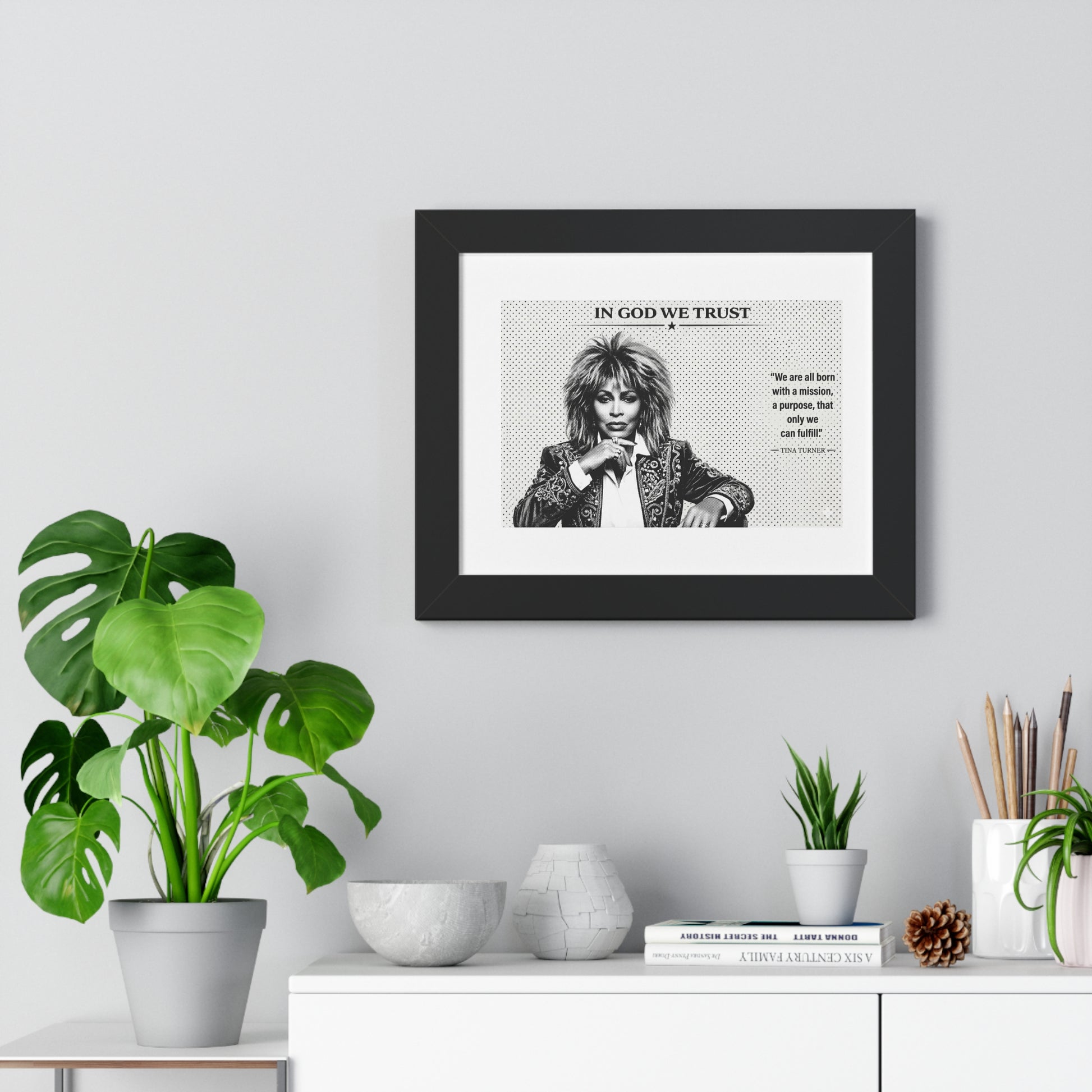 Framed artwork with a quote on a wall above a white cabinet with decorative items.