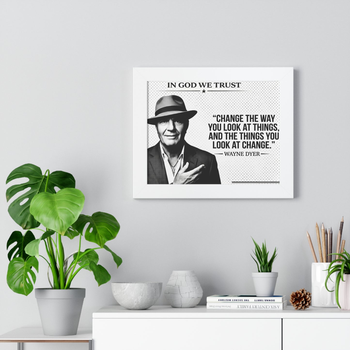 Framed portrait of a man with a quote on a wall above a desk with plants and decor.