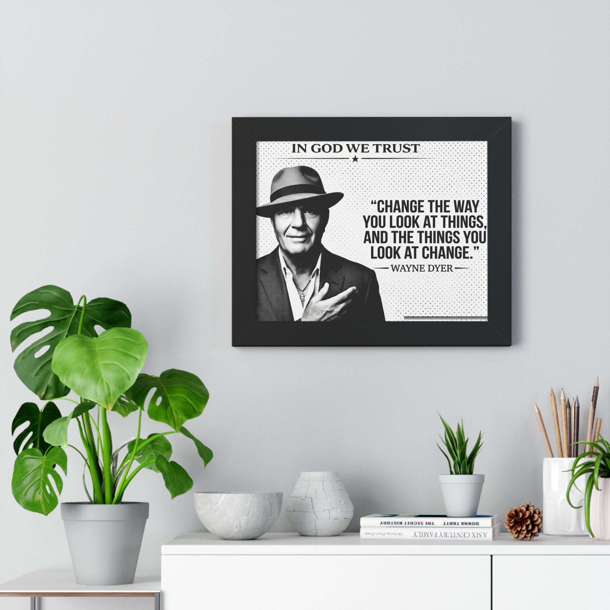 Framed portrait of a man with a quote on a wall above a white cabinet with decorative items.